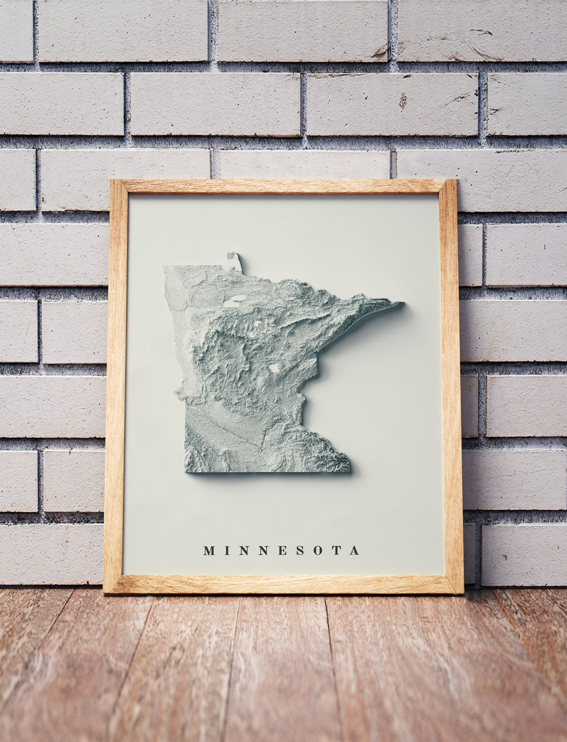 Minnesota shaded relief map in a wooden frame. Realistic terrain art print for home decor, displayed against a brick wall