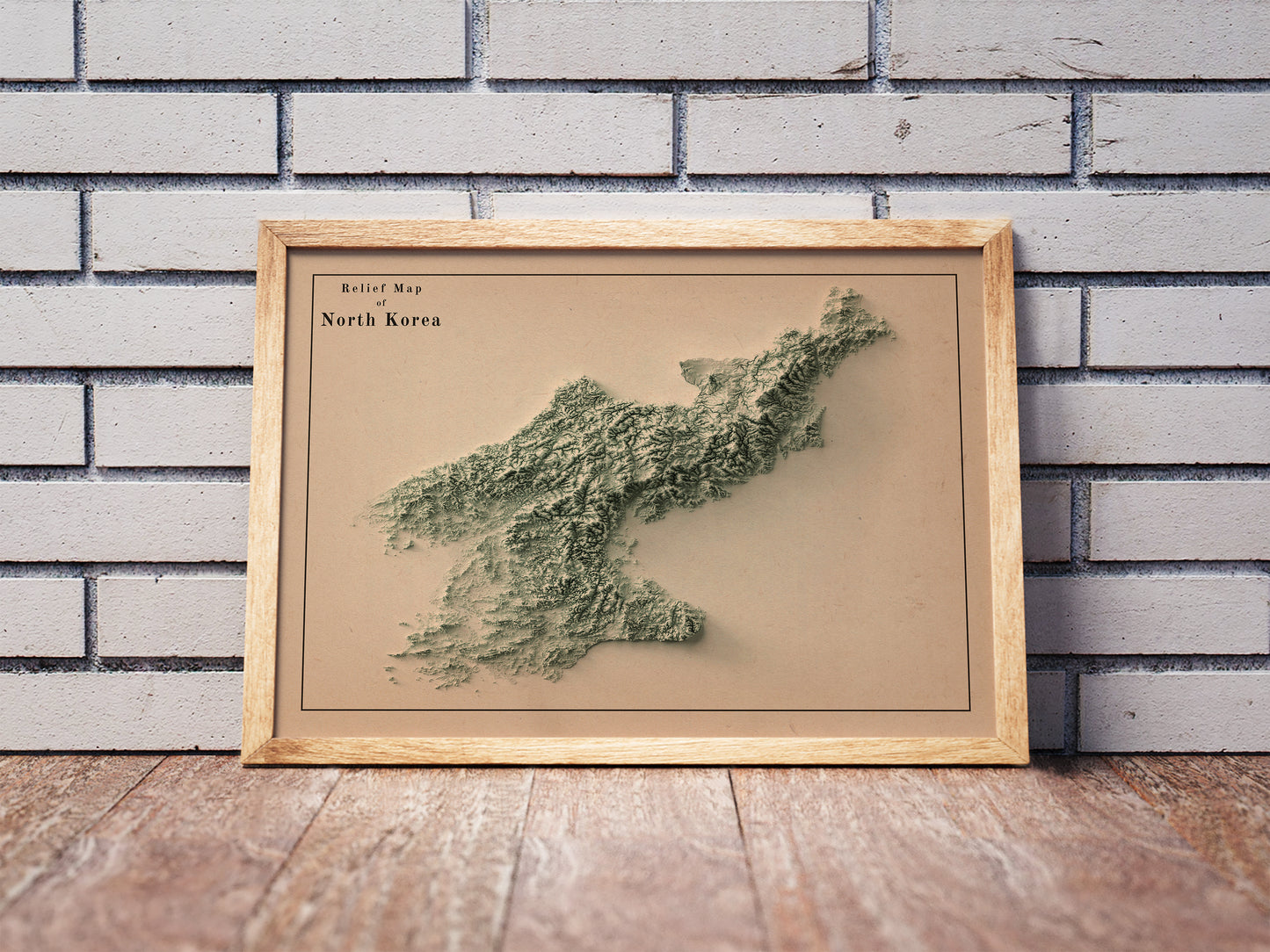 Vintage North Korea shaded relief map in a wooden frame. Realistic terrain art print for home decor, displayed against a brick wall