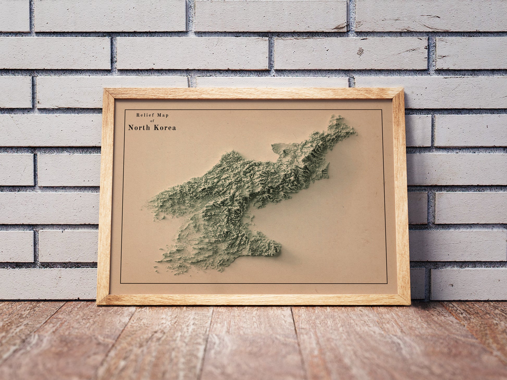 Vintage North Korea shaded relief map in a wooden frame. Realistic terrain art print for home decor, displayed against a brick wall