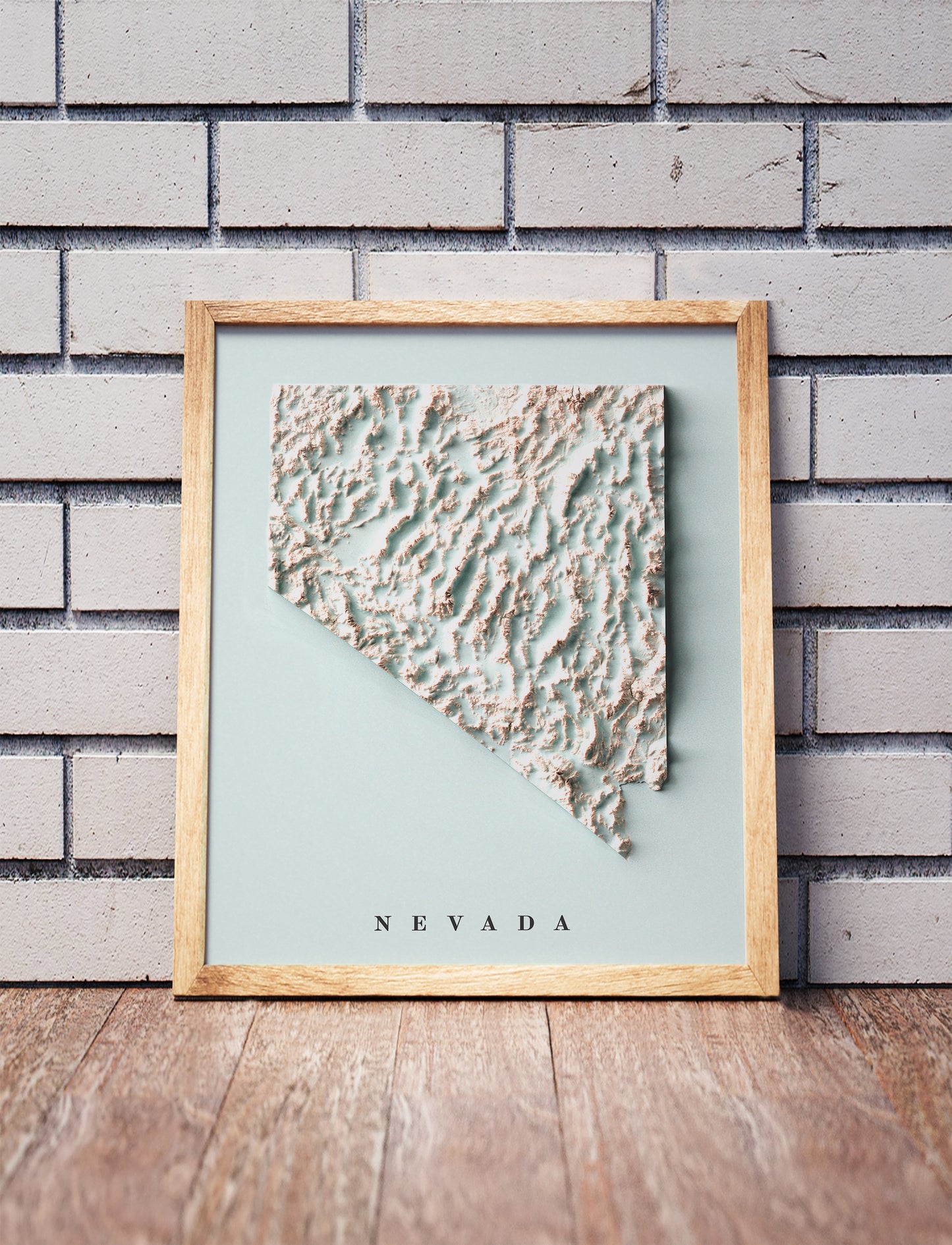 Nevada shaded relief map in a wooden frame. Realistic terrain art print for home decor, displayed against a brick wall