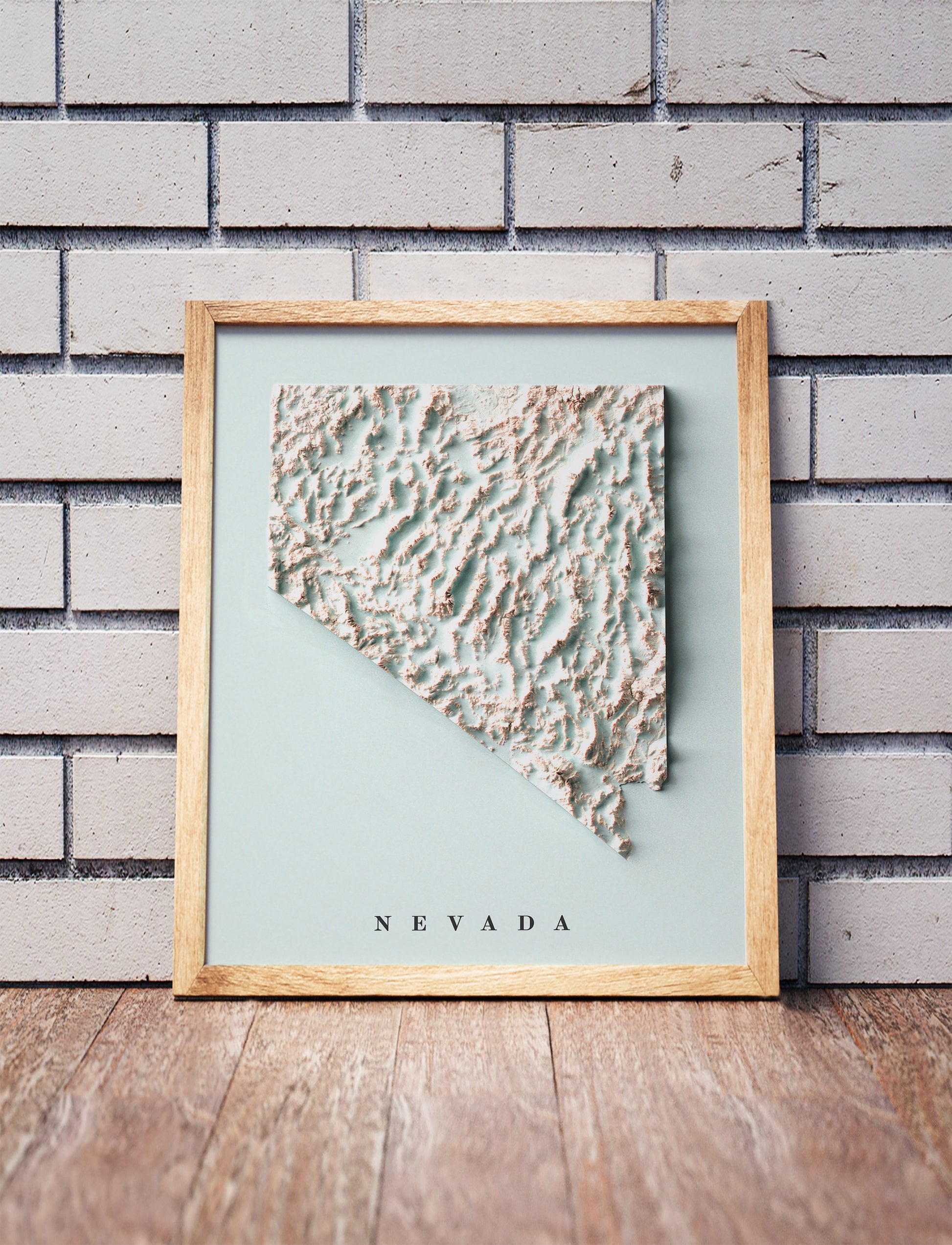 Nevada shaded relief map in a wooden frame. Realistic terrain art print for home decor, displayed against a brick wall