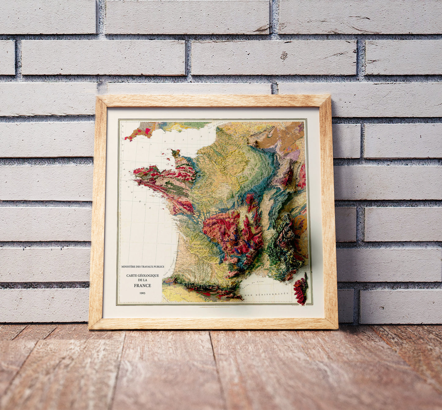 Vintage France shaded relief map in a wooden frame. Realistic terrain art print for home decor, displayed against a brick wall