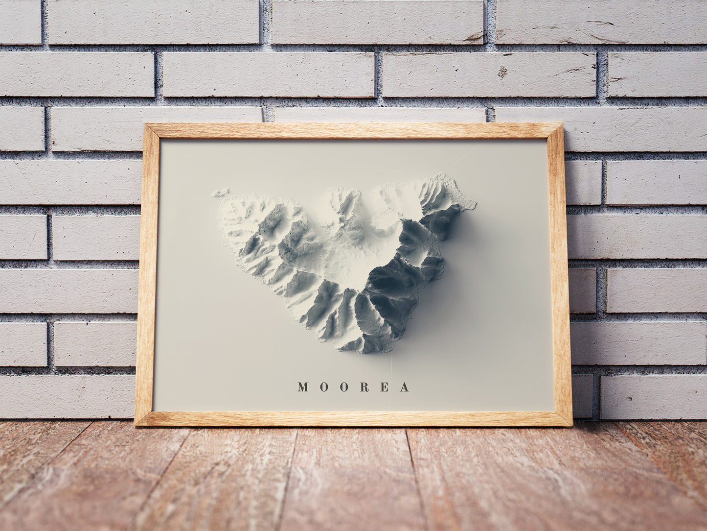 Moorea shaded relief map in a wooden frame. Realistic terrain art print for home decor, displayed against a brick wall