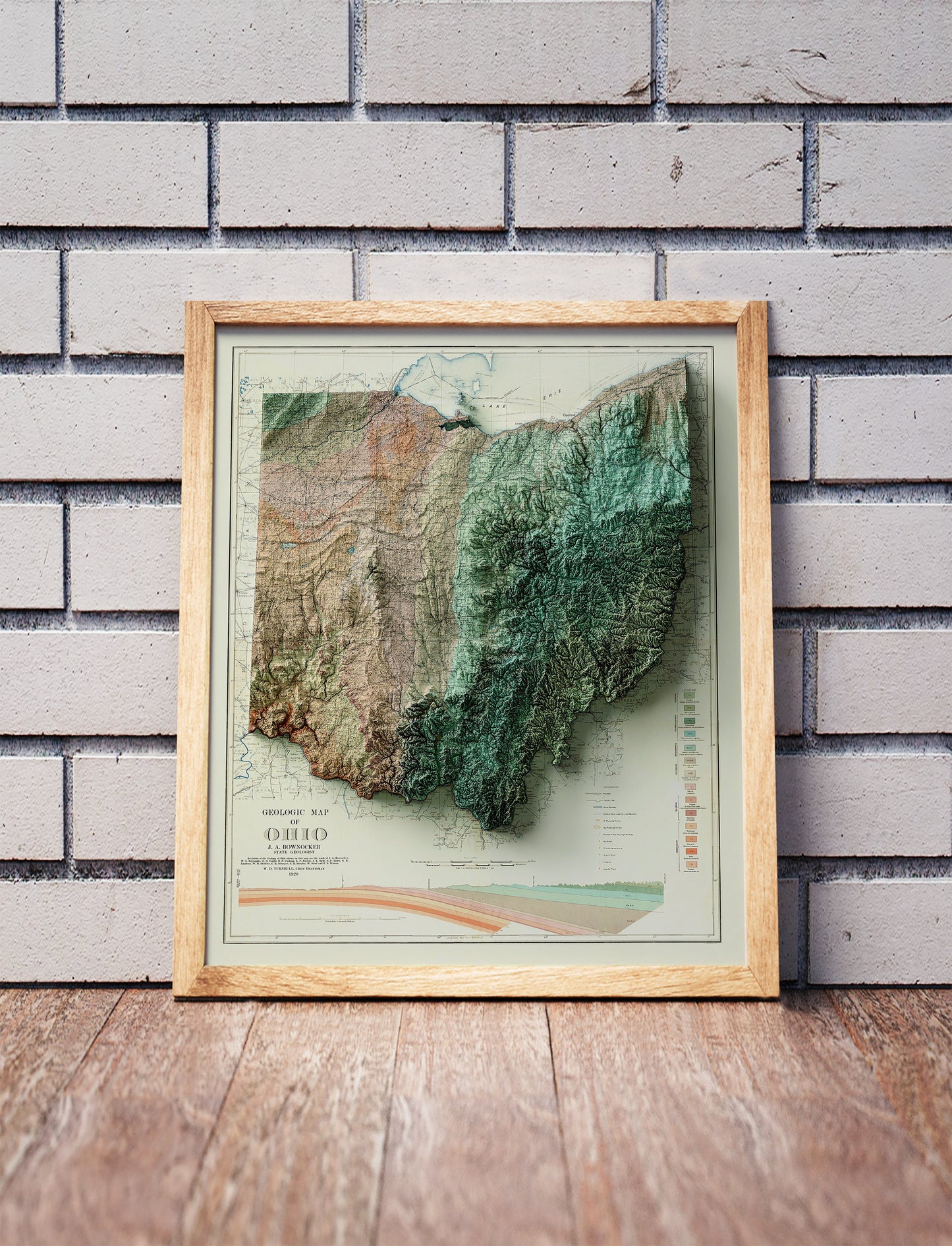 Vintage Ohio shaded relief map in a wooden frame. Realistic terrain art print for home decor, displayed against a brick wall