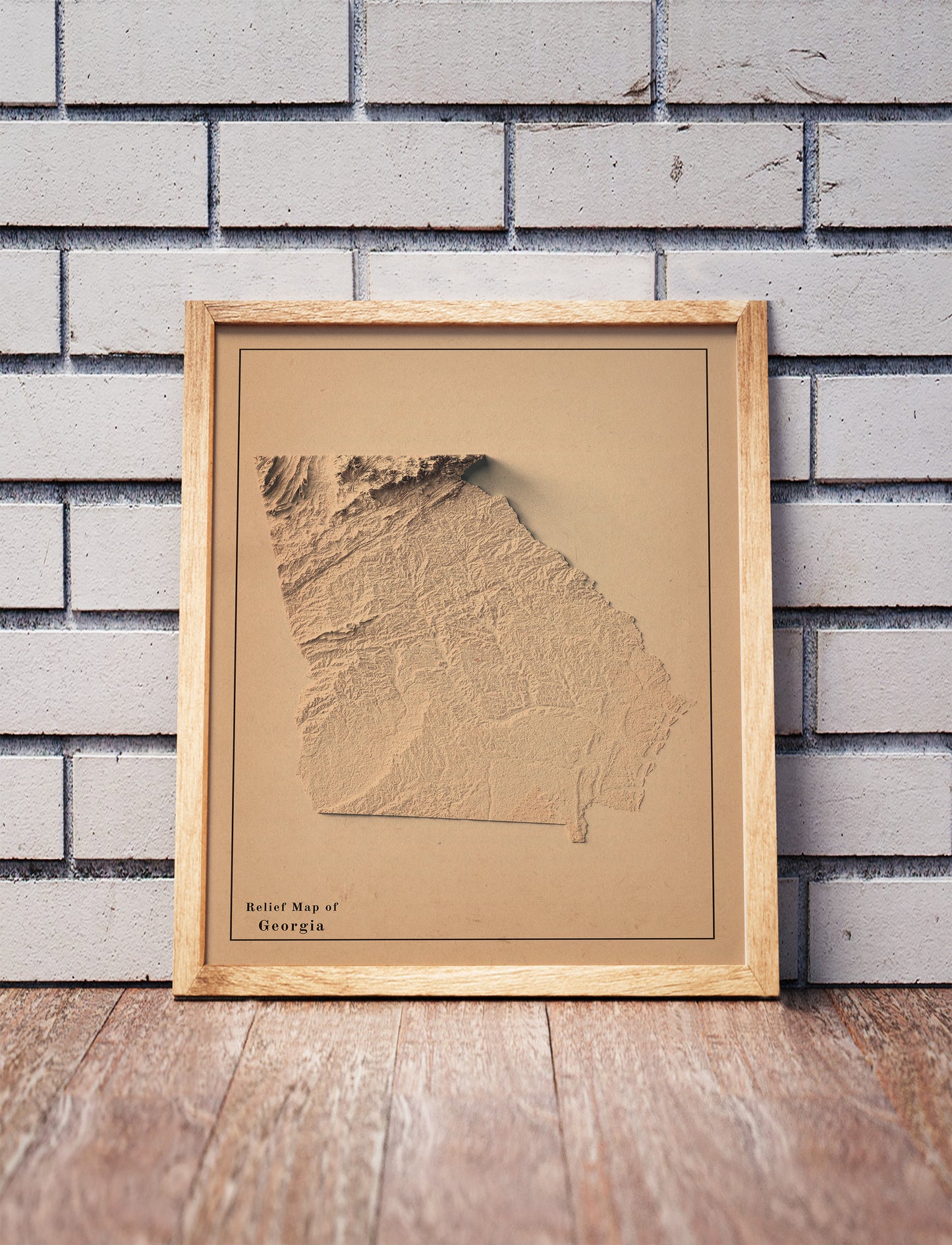 Vintage Georgia shaded relief map in a wooden frame. Realistic terrain art print for home decor, displayed against a brick wall