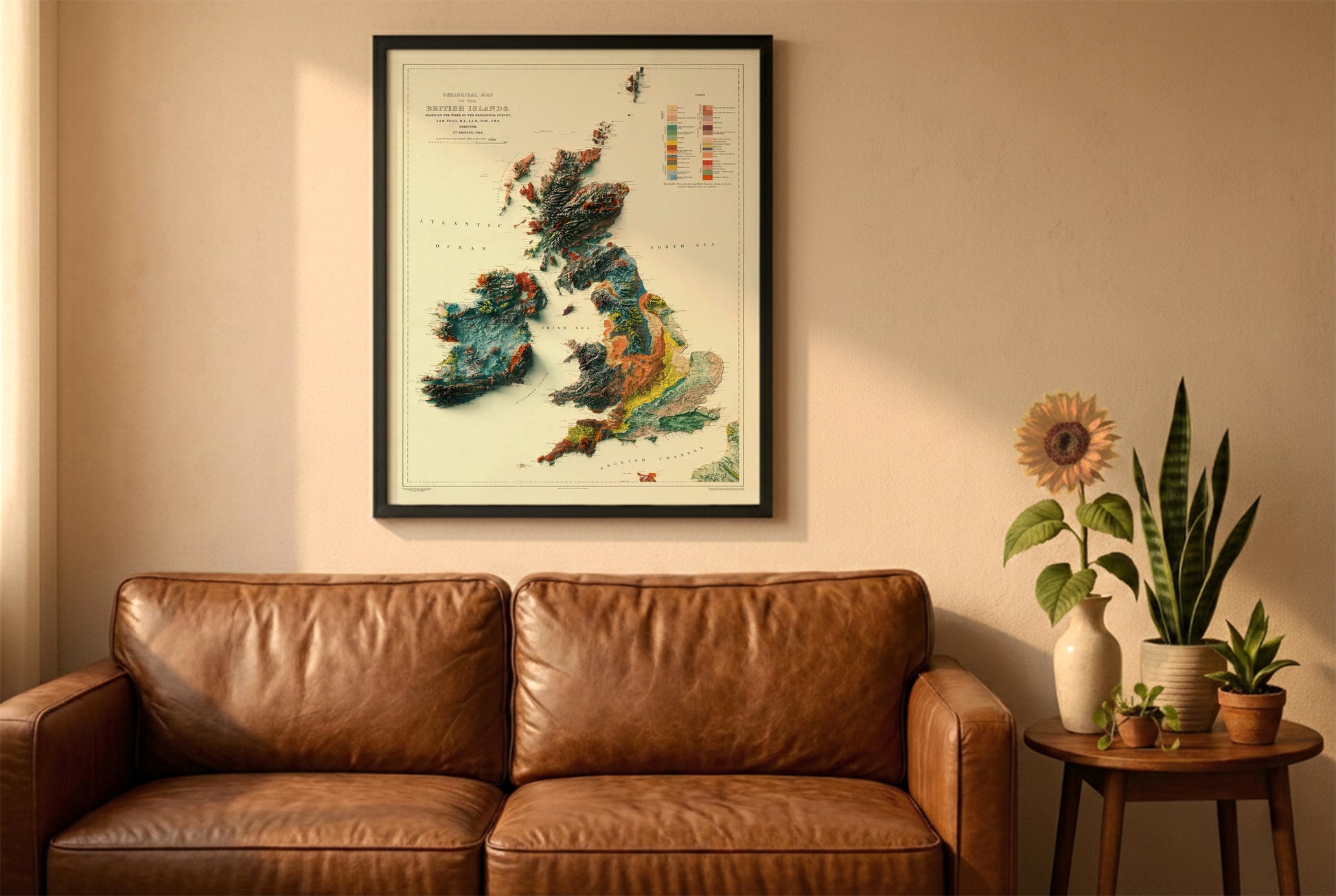 England Ireland Wales Scotland vintage relief map in a black frame above a brown leather sofa. Boho living room with warm sunlight, sunflower, and indoor plants on a wooden side table