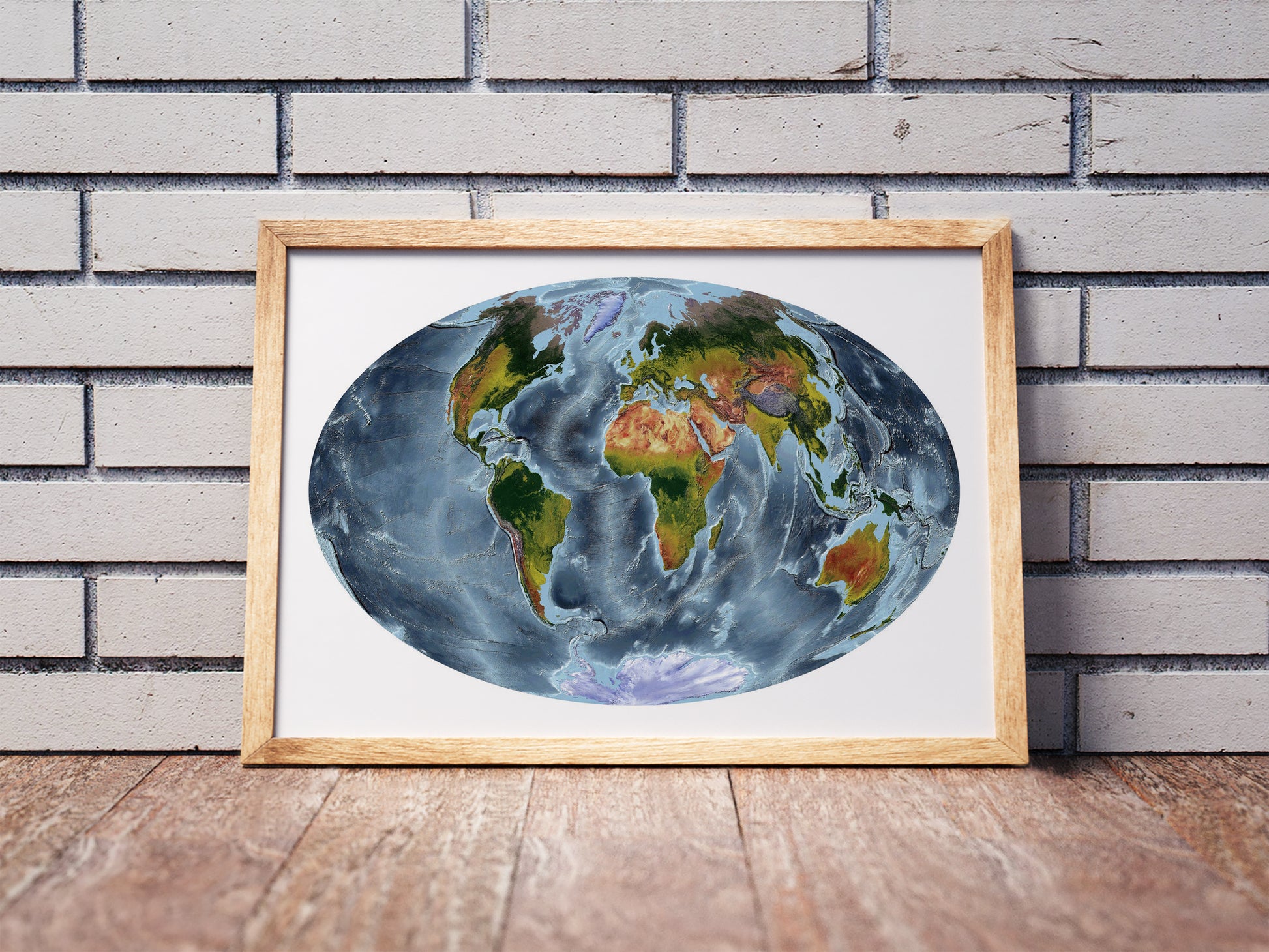 Aitoff projection shaded relief world map in a wooden frame. Realistic terrain art print for home decor, displayed against a brick wall