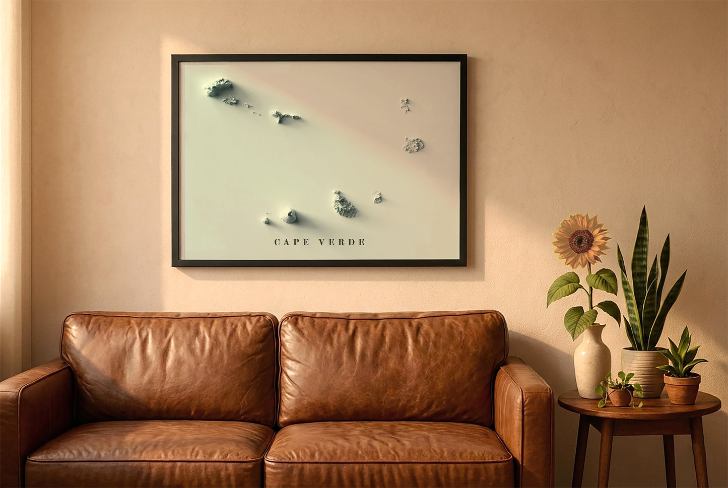 Cape Verde relief map in a black frame above a brown leather sofa. Boho living room with warm sunlight, sunflower, and indoor plants on a wooden side table