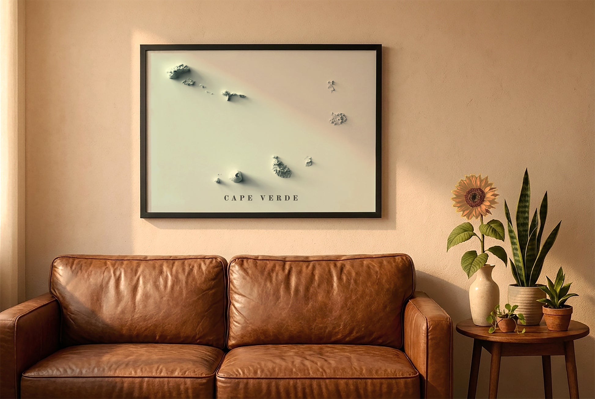 Cape Verde relief map in a black frame above a brown leather sofa. Boho living room with warm sunlight, sunflower, and indoor plants on a wooden side table
