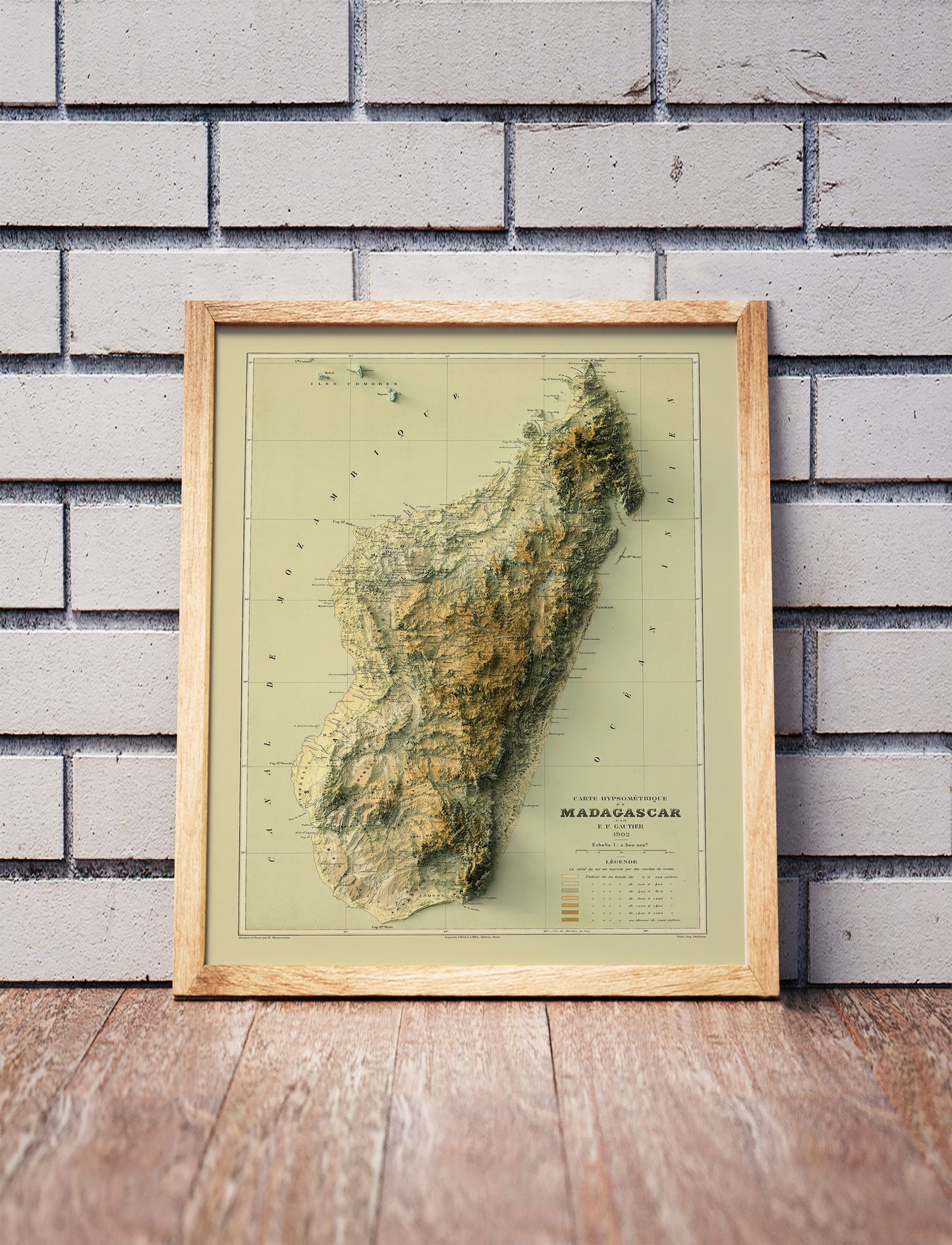 Vintage Madagascar shaded relief map in a wooden frame. Realistic terrain art print for home decor, displayed against a brick wall