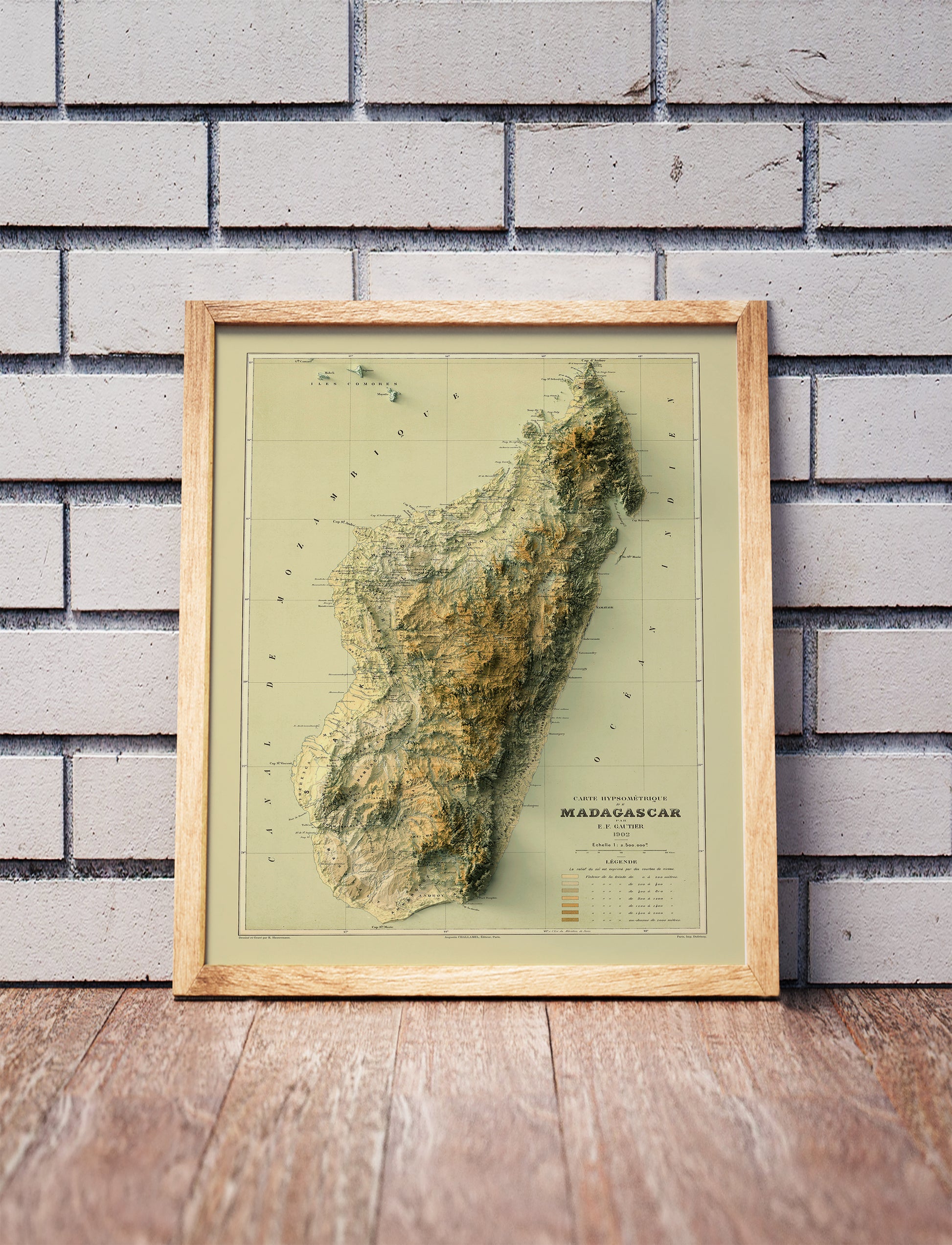 Vintage Madagascar shaded relief map in a wooden frame. Realistic terrain art print for home decor, displayed against a brick wall