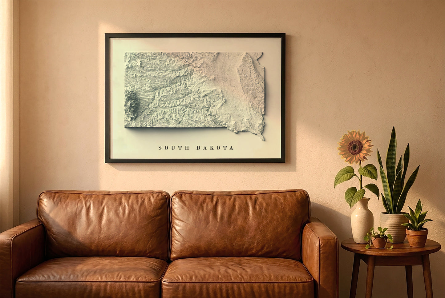 South Dakota relief map in a black frame above a brown leather sofa. Boho living room with warm sunlight, sunflower, and indoor plants on a wooden side table