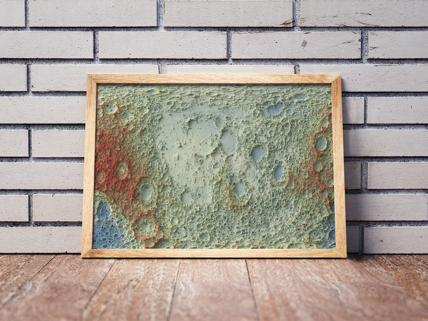 Moon shaded relief map in a wooden frame. Realistic terrain art print for home decor, displayed against a brick wall