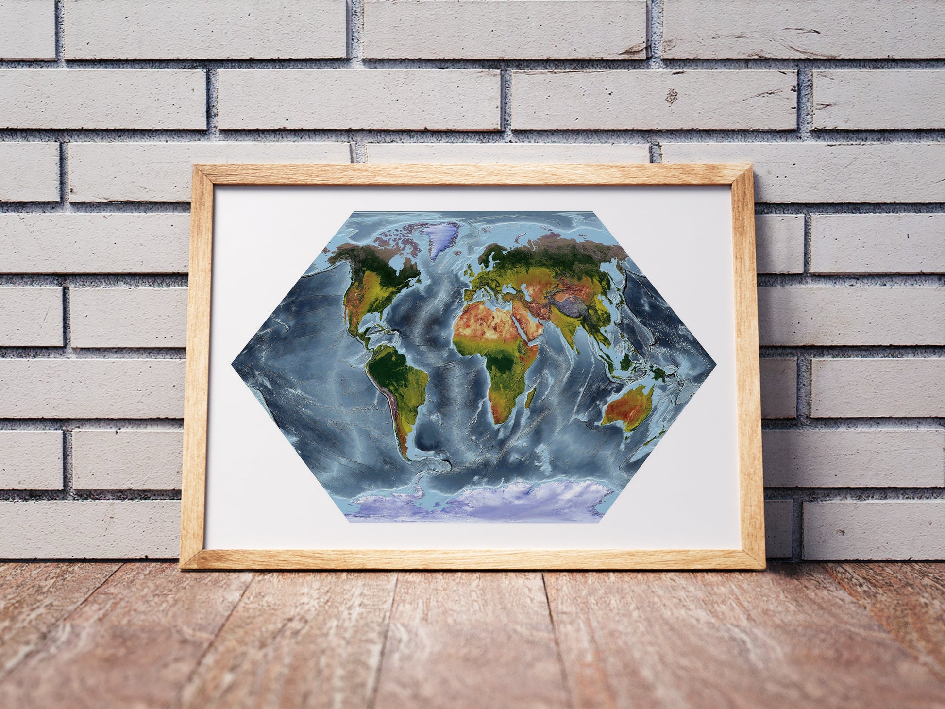 Eckert projection shaded relief world map in a wooden frame. Realistic terrain art print for home decor, displayed against a brick wall