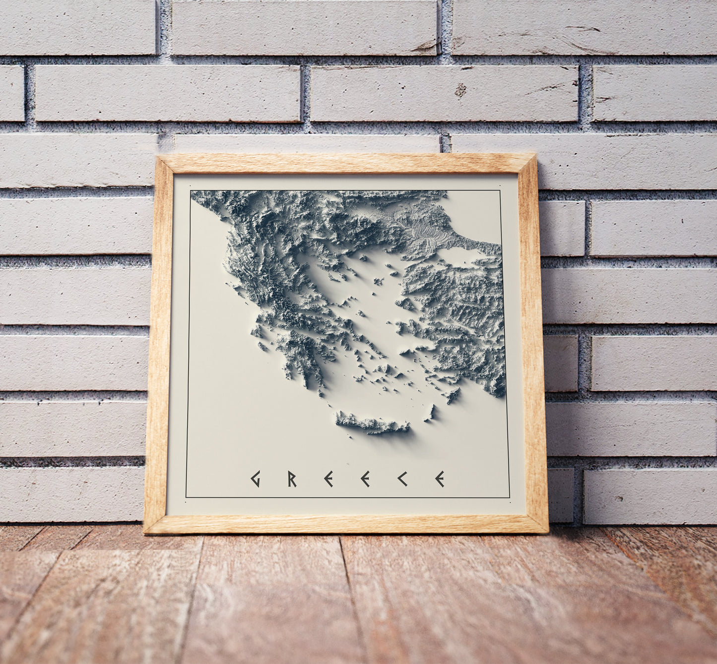 Greece shaded relief map in a wooden frame. Realistic terrain art print for home decor, displayed against a brick wall