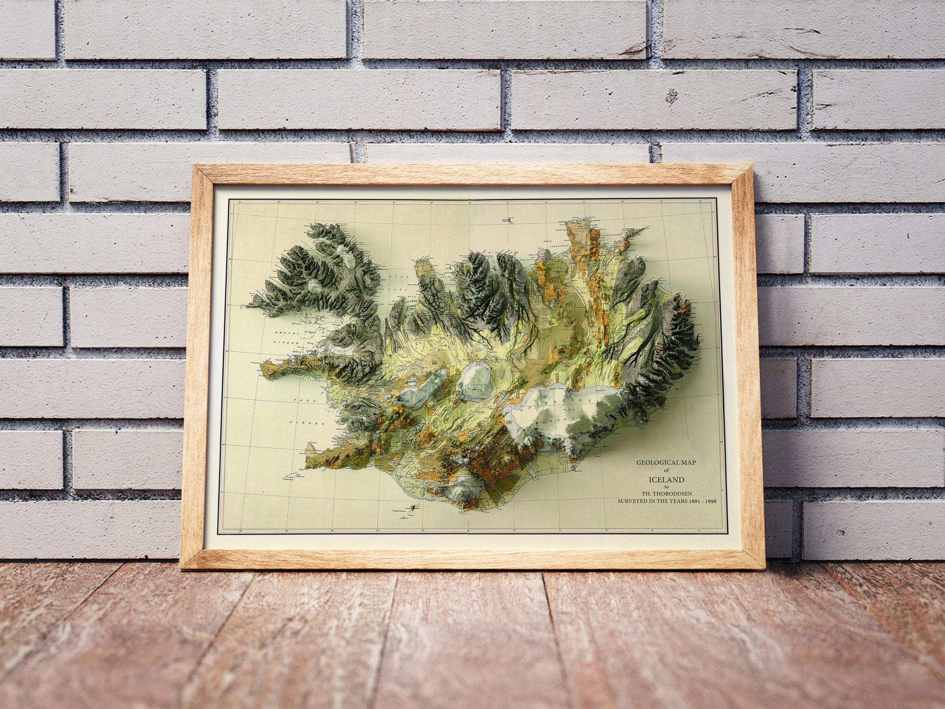 Vintage Iceland shaded relief map in a wooden frame. Realistic terrain art print for home decor, displayed against a brick wall