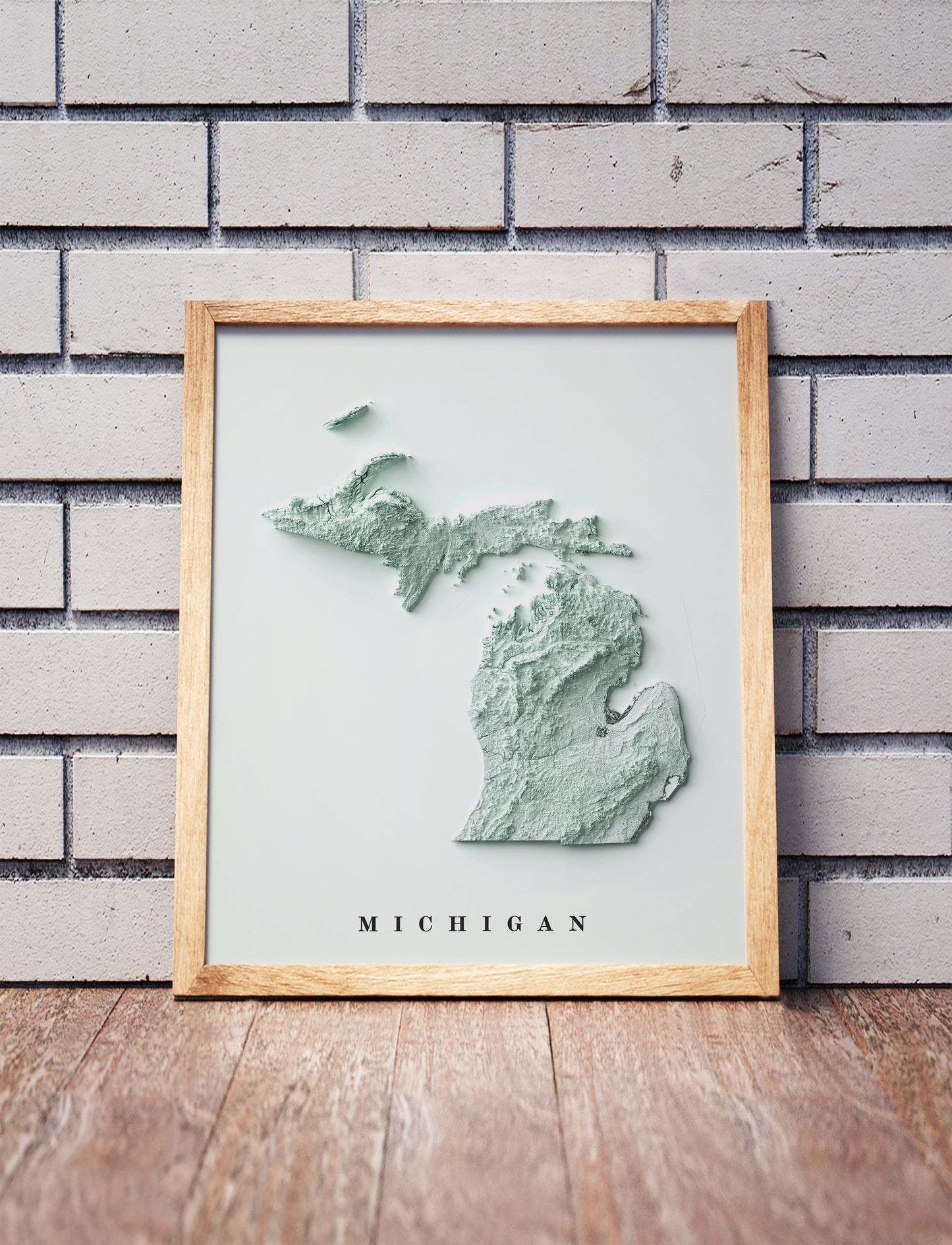 Michigan shaded relief map in a wooden frame. Realistic terrain art print for home decor, displayed against a brick wall
