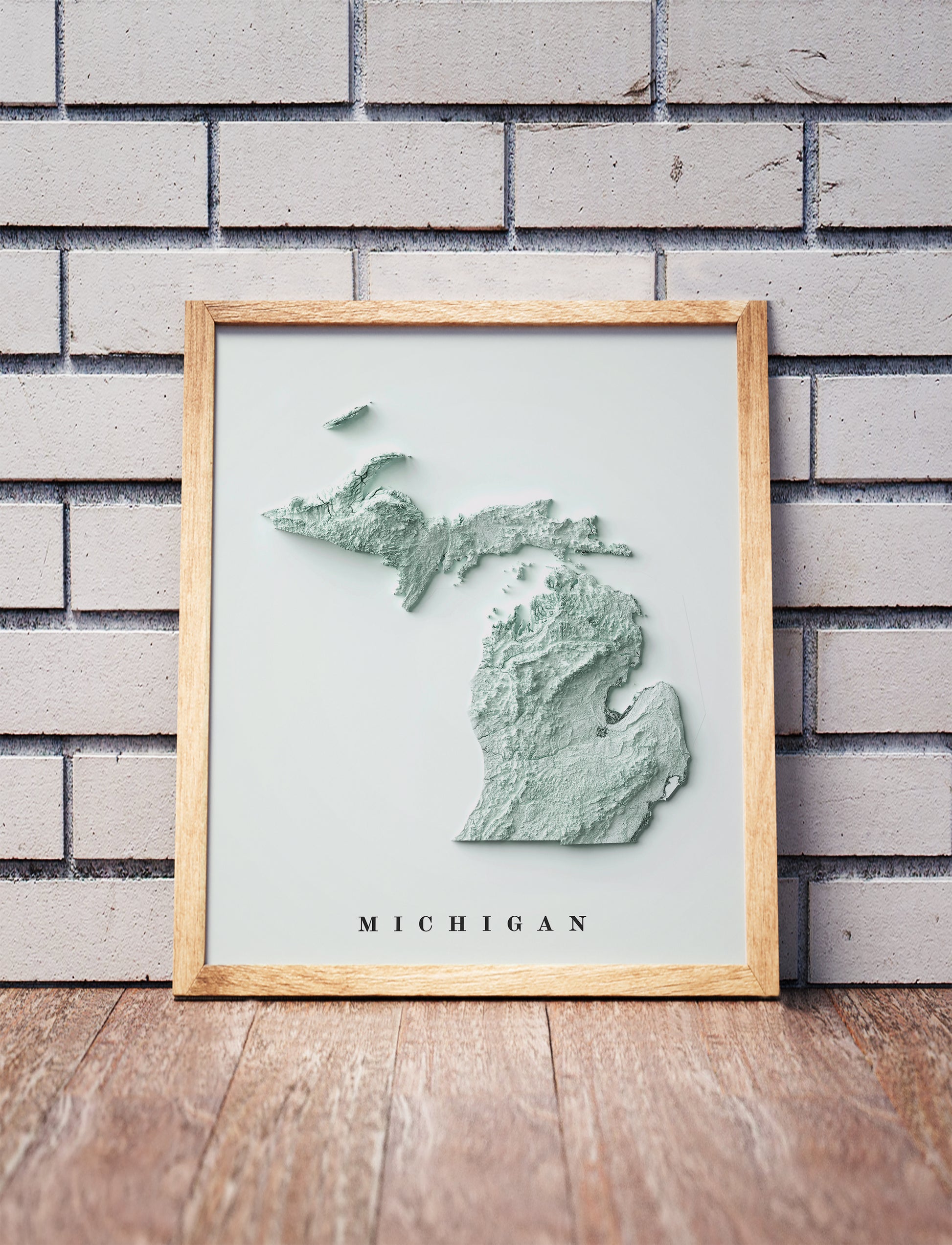 Michigan shaded relief map in a wooden frame. Realistic terrain art print for home decor, displayed against a brick wall