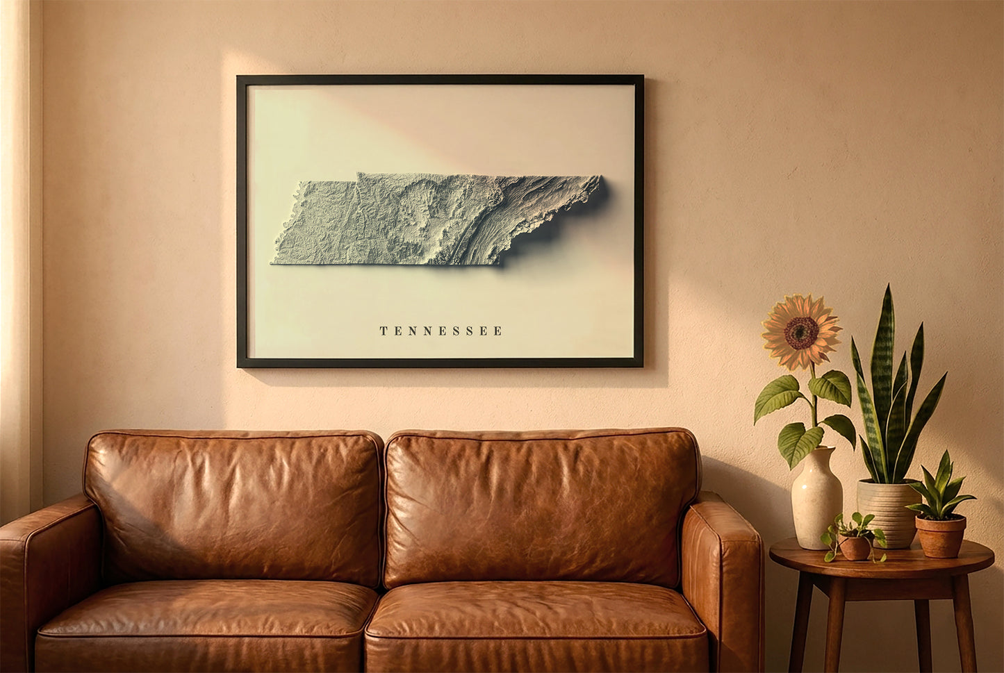 Tennessee relief map in a black frame above a brown leather sofa. Boho living room with warm sunlight, sunflower, and indoor plants on a wooden side table