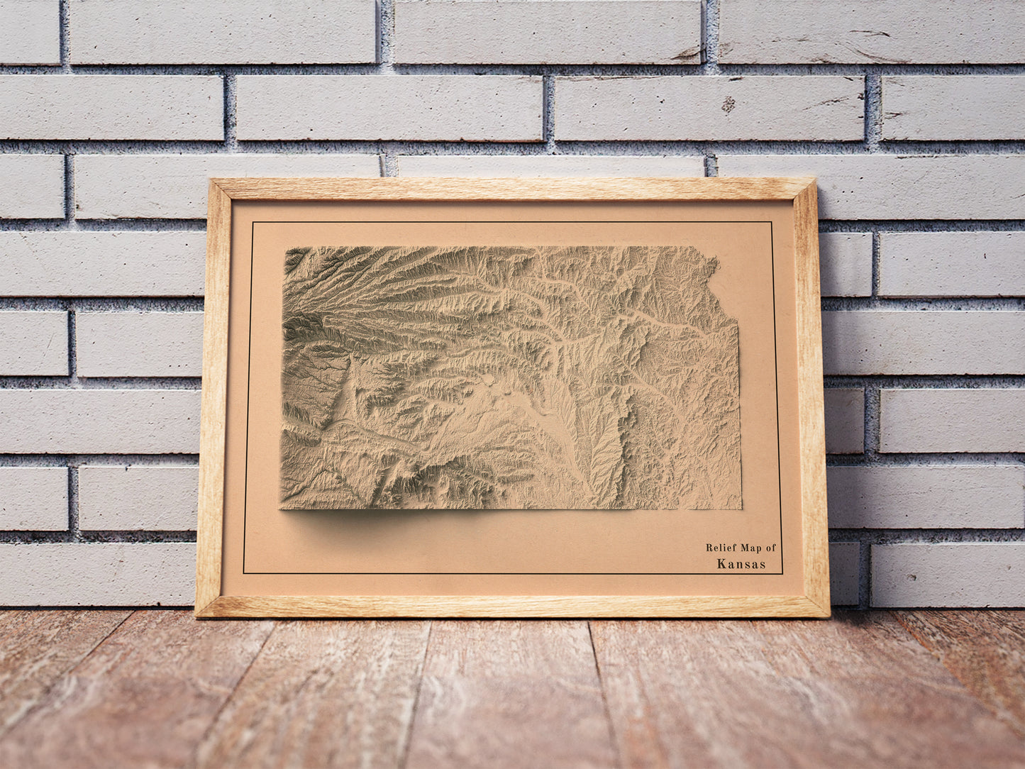 Vintage Kansas shaded relief map in a wooden frame. Realistic terrain art print for home decor, displayed against a brick wall