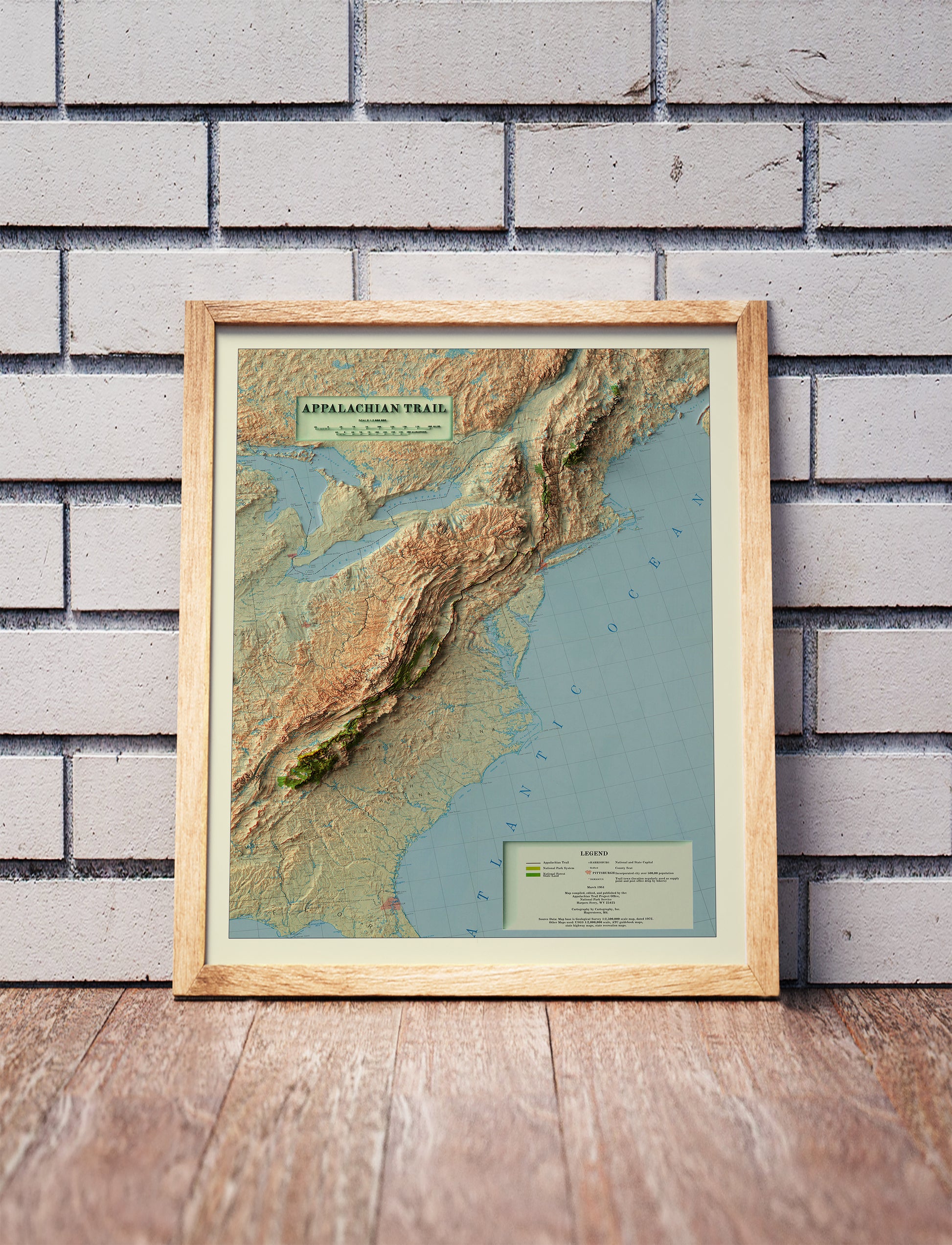 Vintage Appalachian Trail shaded relief map in a wooden frame. Realistic terrain art print for home decor, displayed against a brick wall
