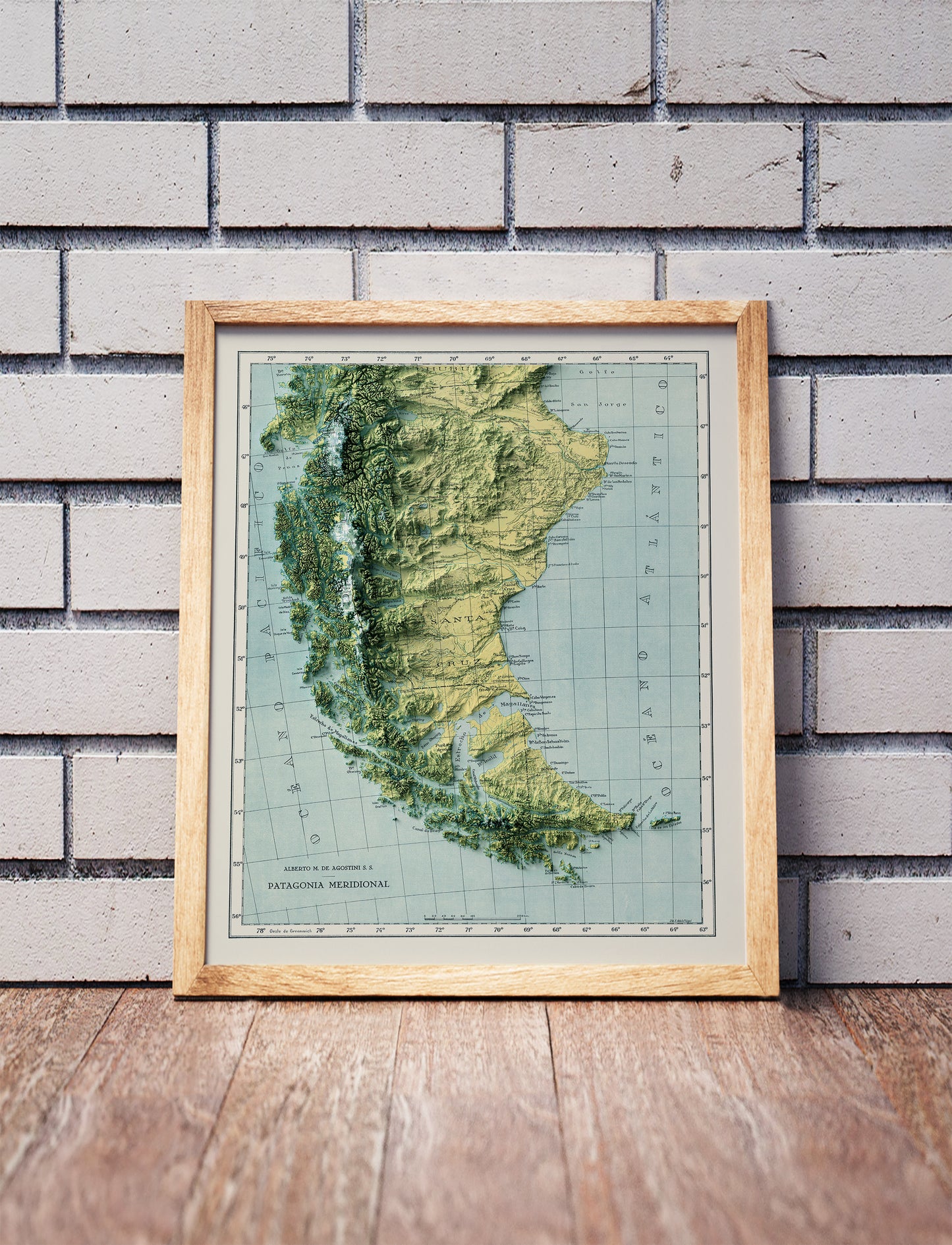 Vintage Patagonia shaded relief map in a wooden frame. Realistic terrain art print for home decor, displayed against a brick wall