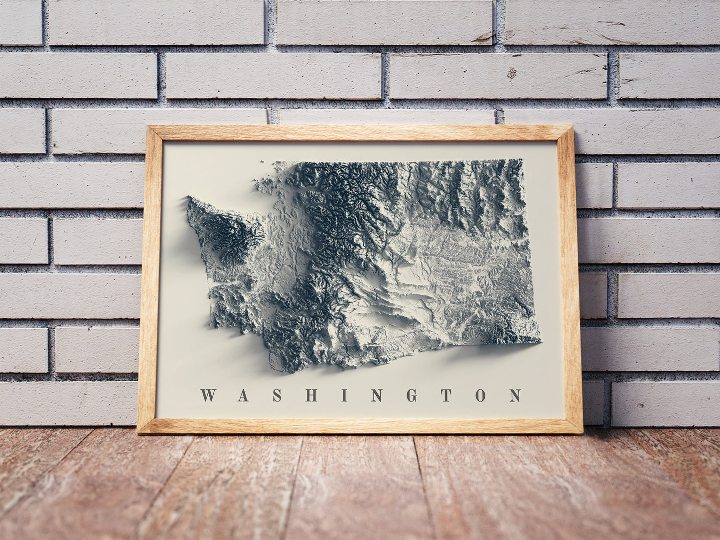 Washington shaded relief map in a wooden frame. Realistic terrain art print for home decor, displayed against a brick wall