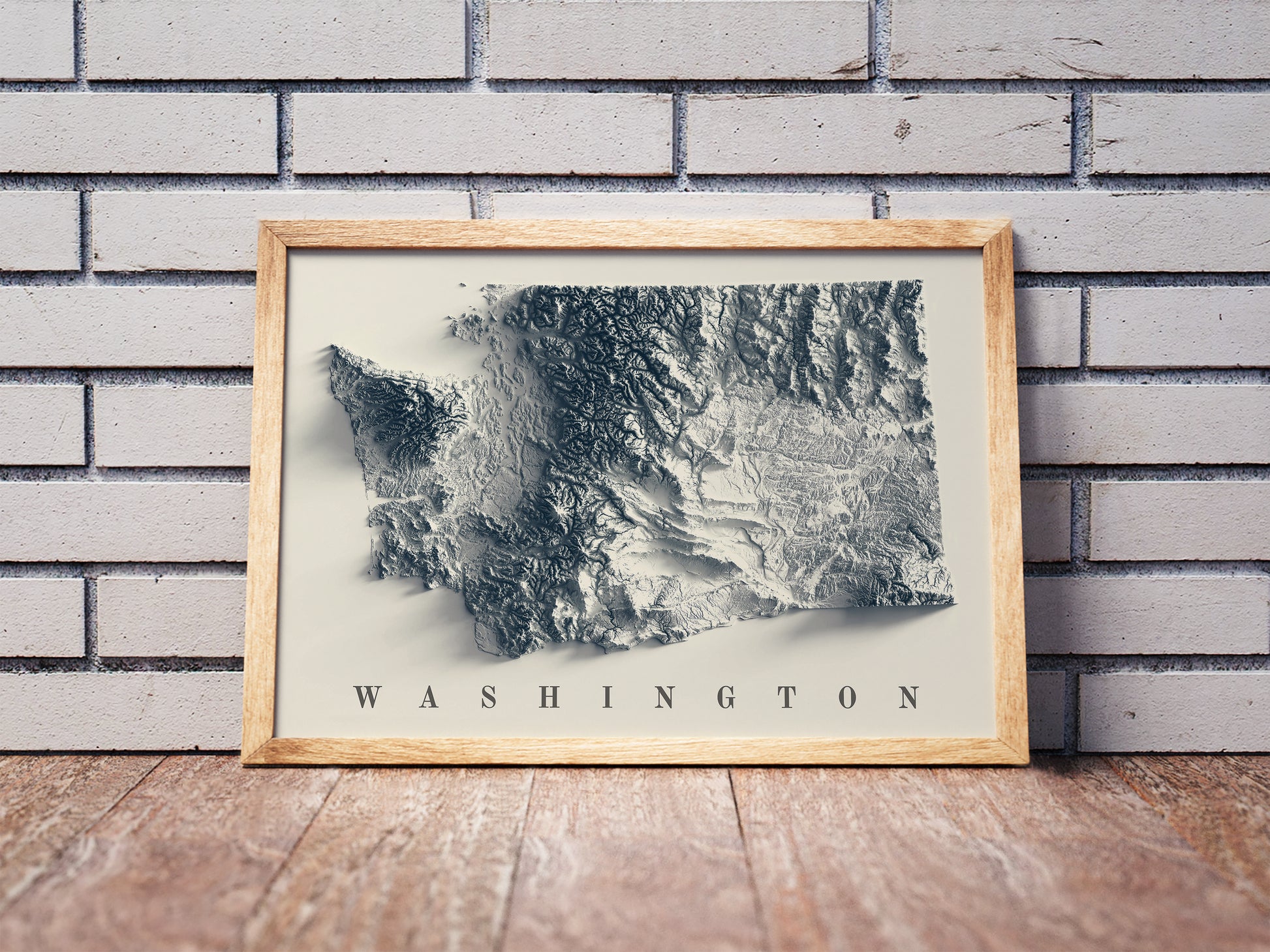 Washington shaded relief map in a wooden frame. Realistic terrain art print for home decor, displayed against a brick wall