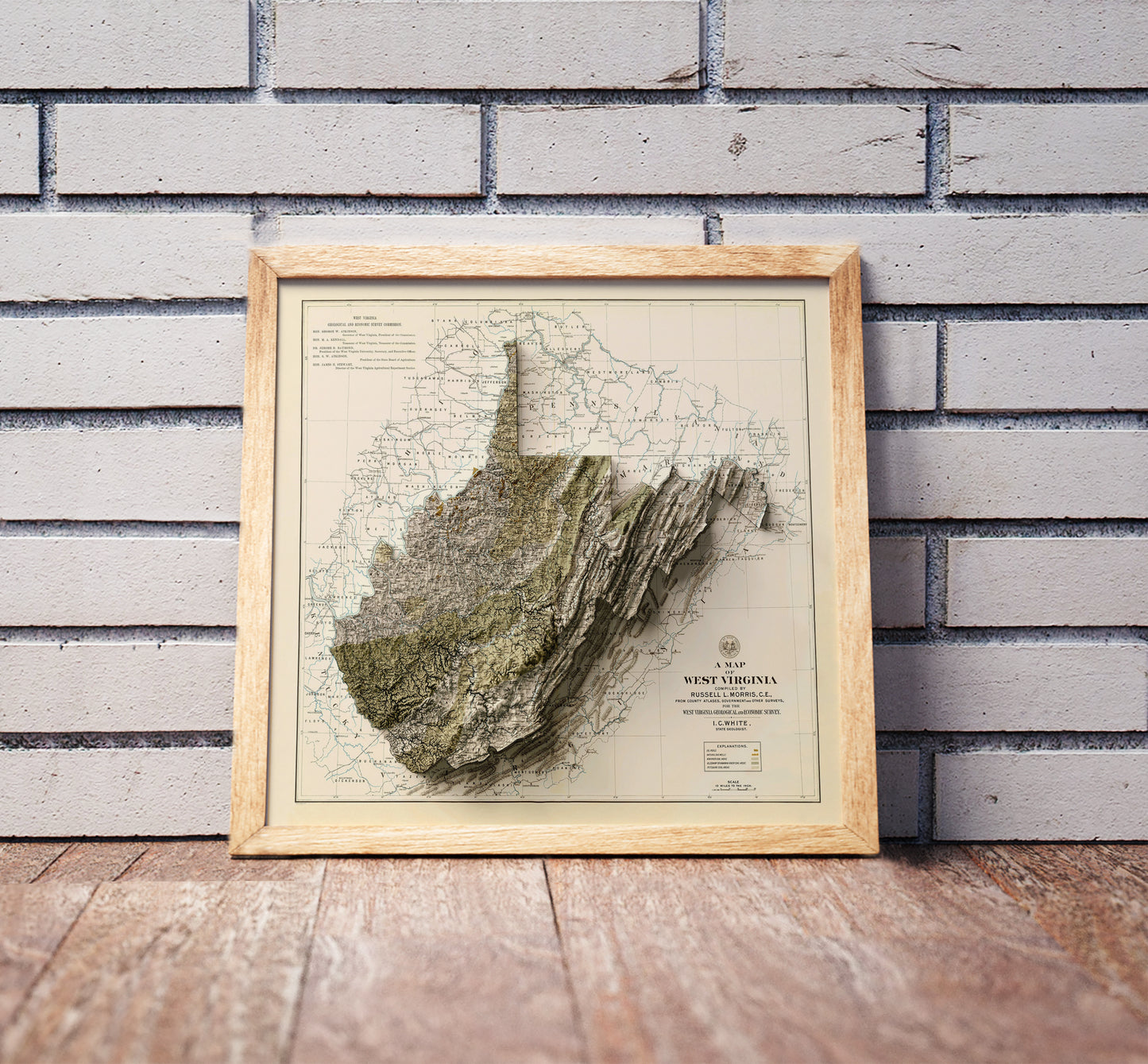 Vintage West Virginia shaded relief map in a wooden frame. Realistic terrain art print for home decor, displayed against a brick wall