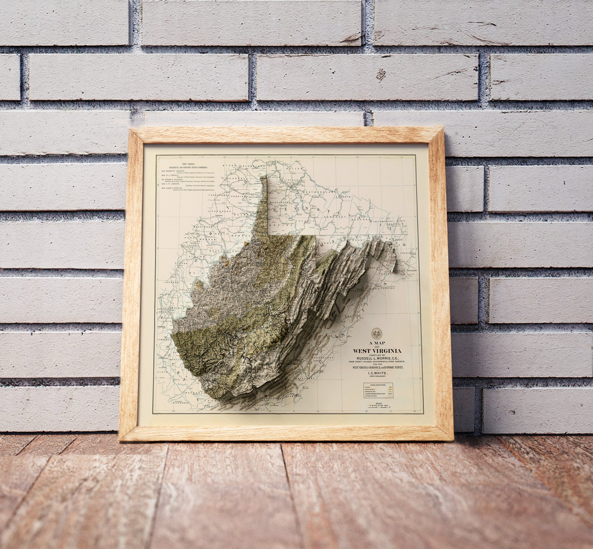 Vintage West Virginia shaded relief map in a wooden frame. Realistic terrain art print for home decor, displayed against a brick wall