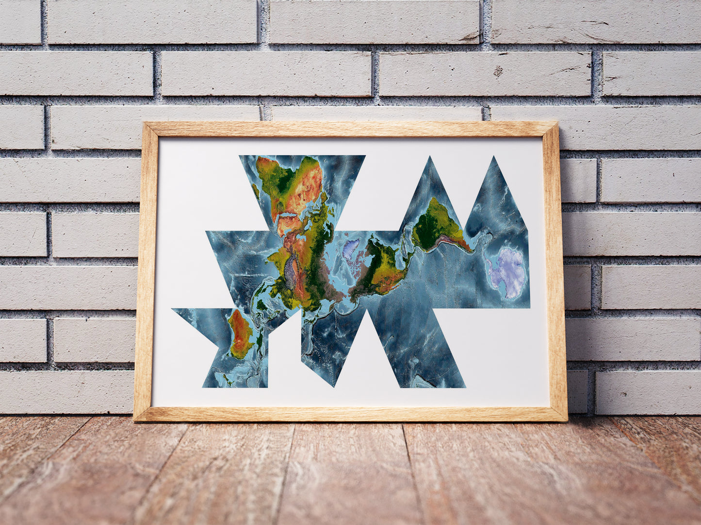 Fuller projection shaded relief world map in a wooden frame. Realistic terrain art print for home decor, displayed against a brick wall