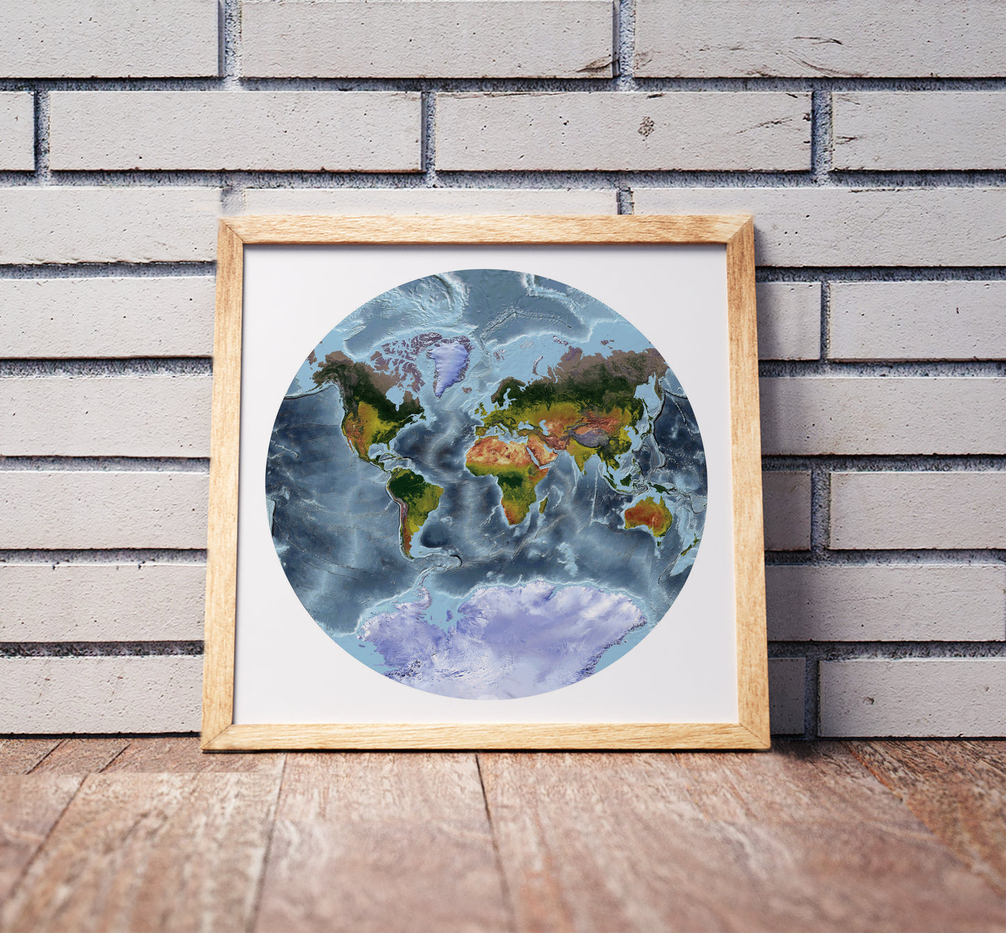 Van der Grinten projection shaded relief world map in a wooden frame. Realistic terrain art print for home decor, displayed against a brick wall