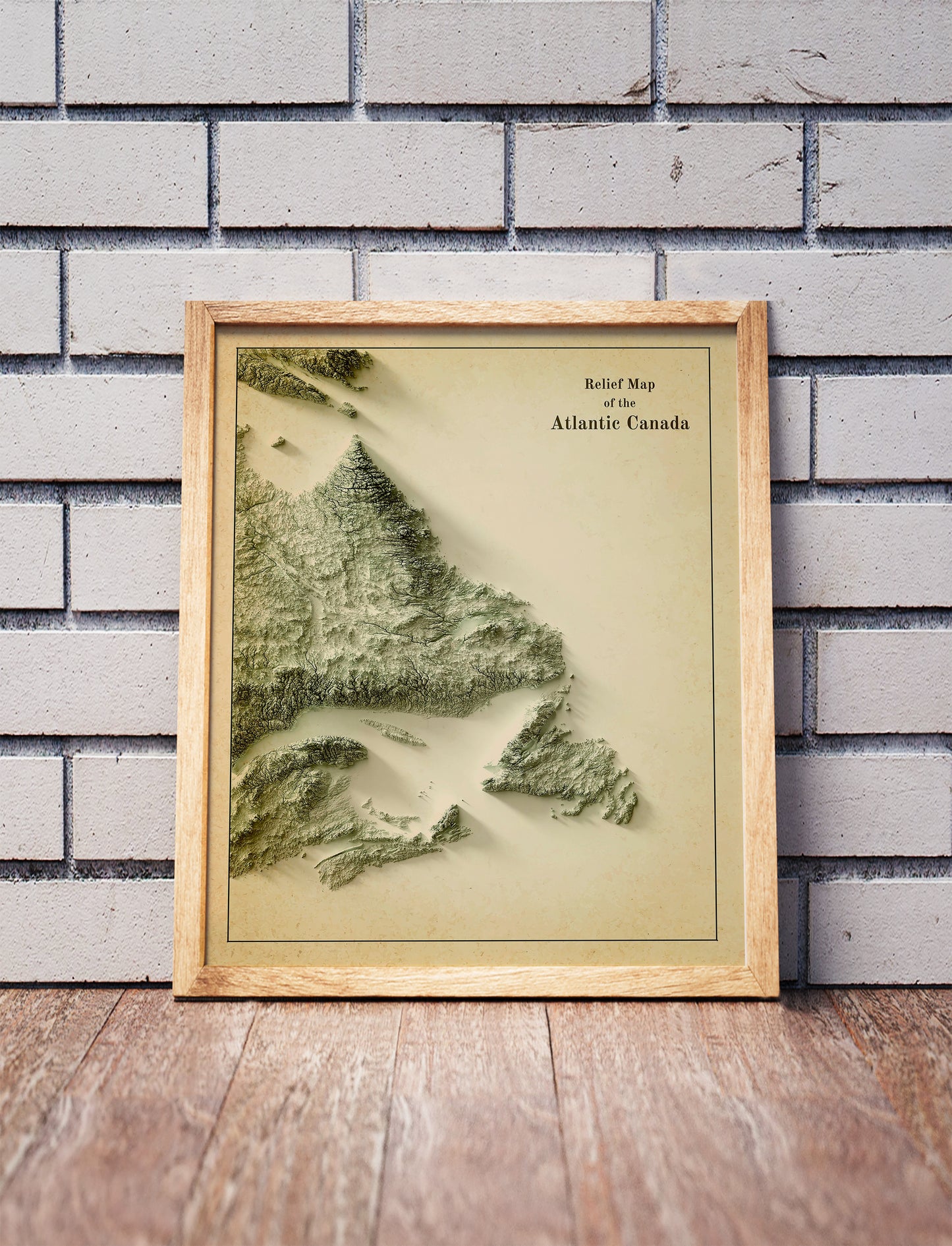 Vintage Atlantic Canada shaded relief map in a wooden frame. Realistic terrain art print for home decor, displayed against a brick wall