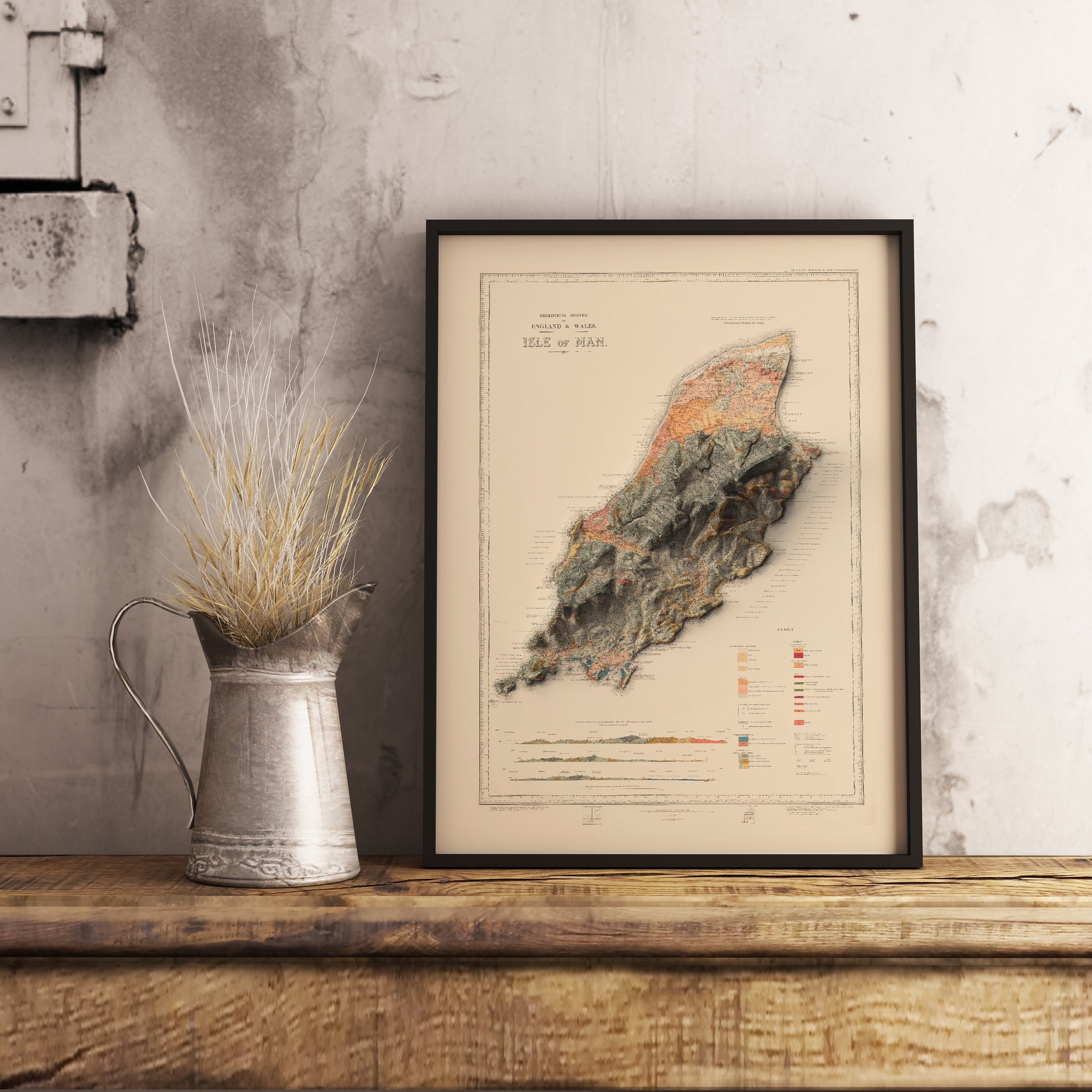 Vintage Isle of Man shaded relief map in black frame. Realistic terrain art print for home decor, displayed on rustic wooden table