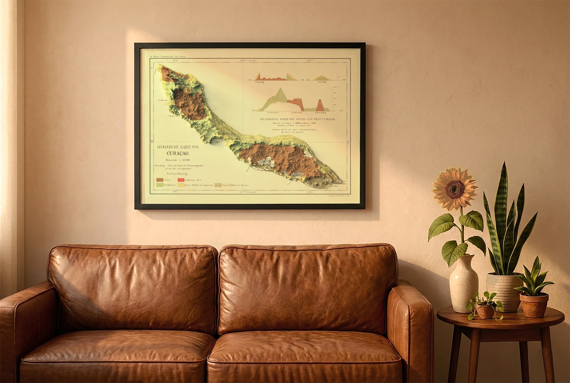 Curaçao vintage relief map in a black frame above a brown leather sofa. Boho living room with warm sunlight, sunflower, and indoor plants on a wooden side table
