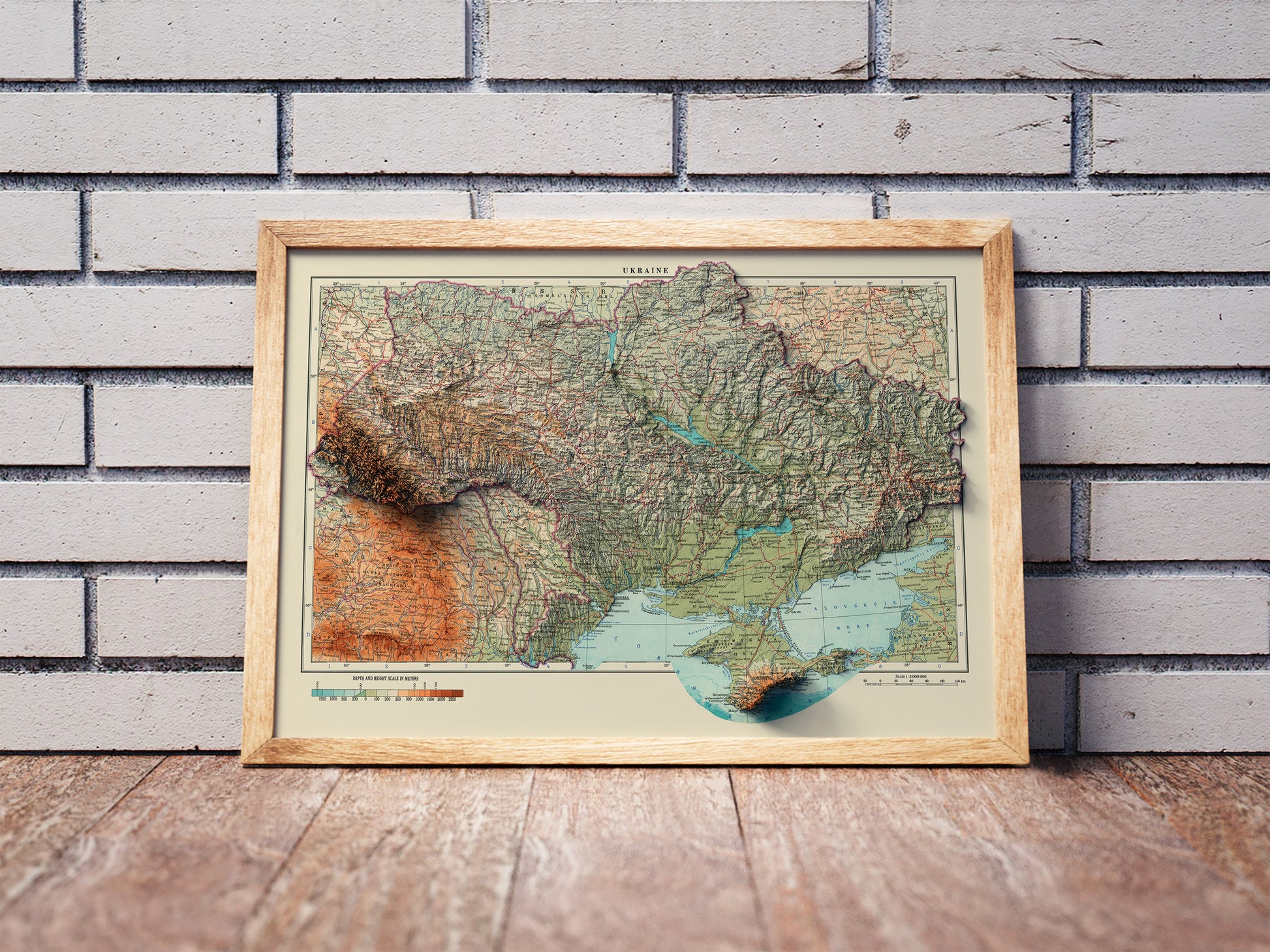 Vintage Ukraine shaded relief map in a wooden frame. Realistic terrain art print for home decor, displayed against a brick wall