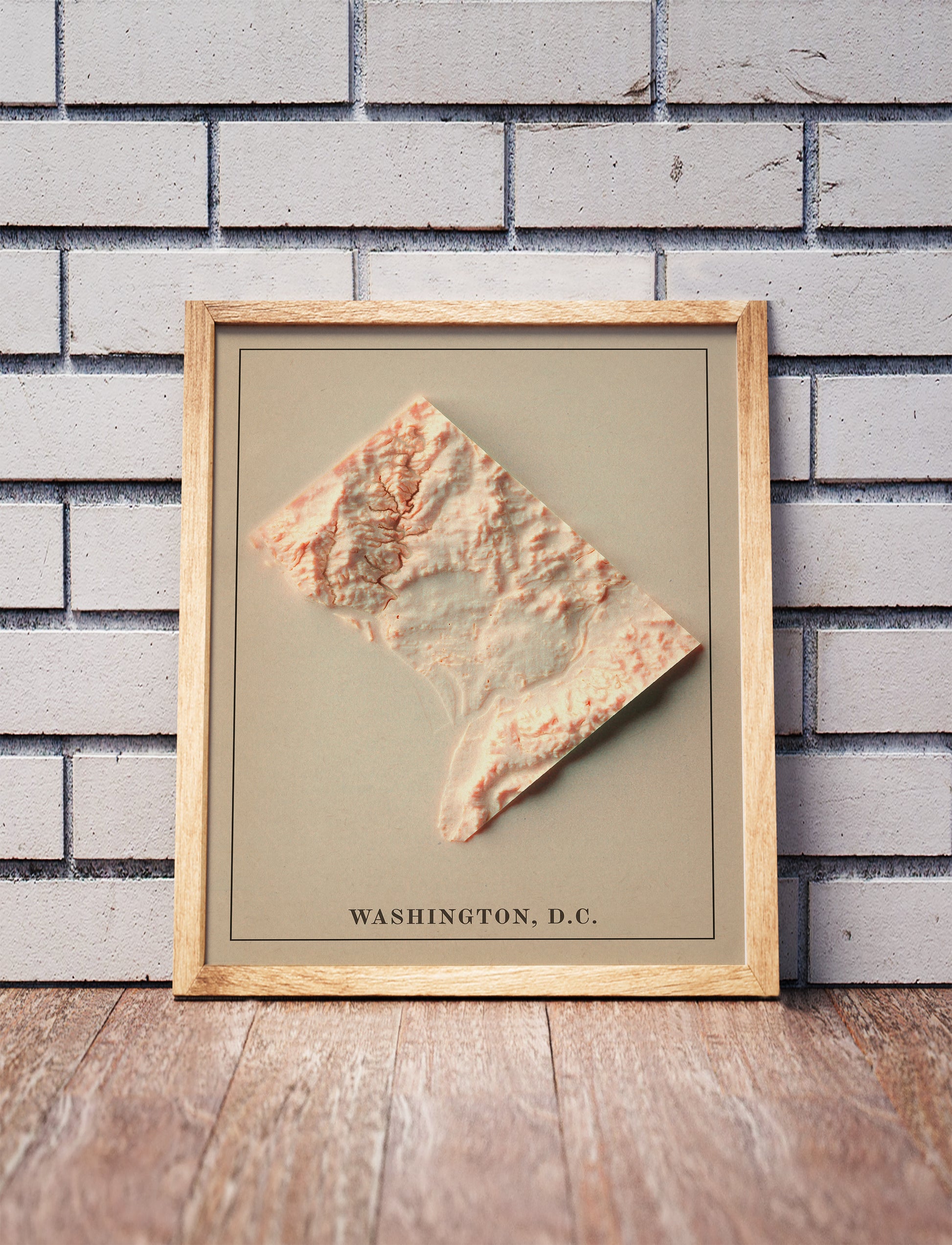 Vintage Washington DC shaded relief map in a wooden frame. Realistic terrain art print for home decor, displayed against a brick wall
