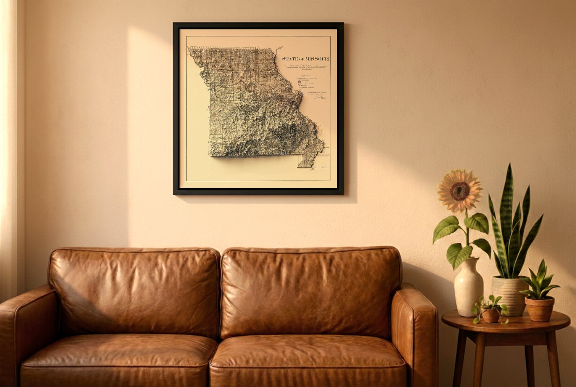 Missouri vintage relief map in a black frame above a brown leather sofa. Boho living room with warm sunlight, sunflower, and indoor plants on a wooden side table