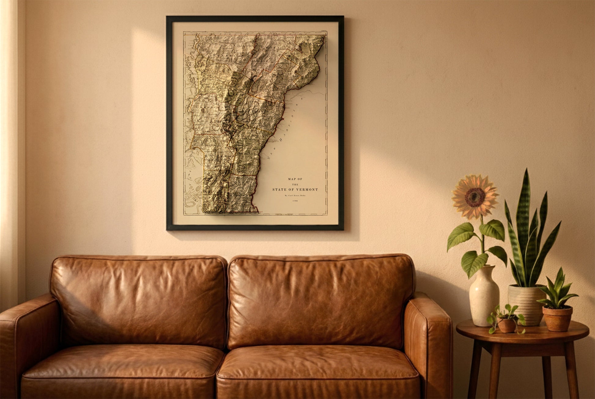 Vermont vintage relief map in a black frame above a brown leather sofa. Boho living room with warm sunlight, sunflower, and indoor plants on a wooden side table