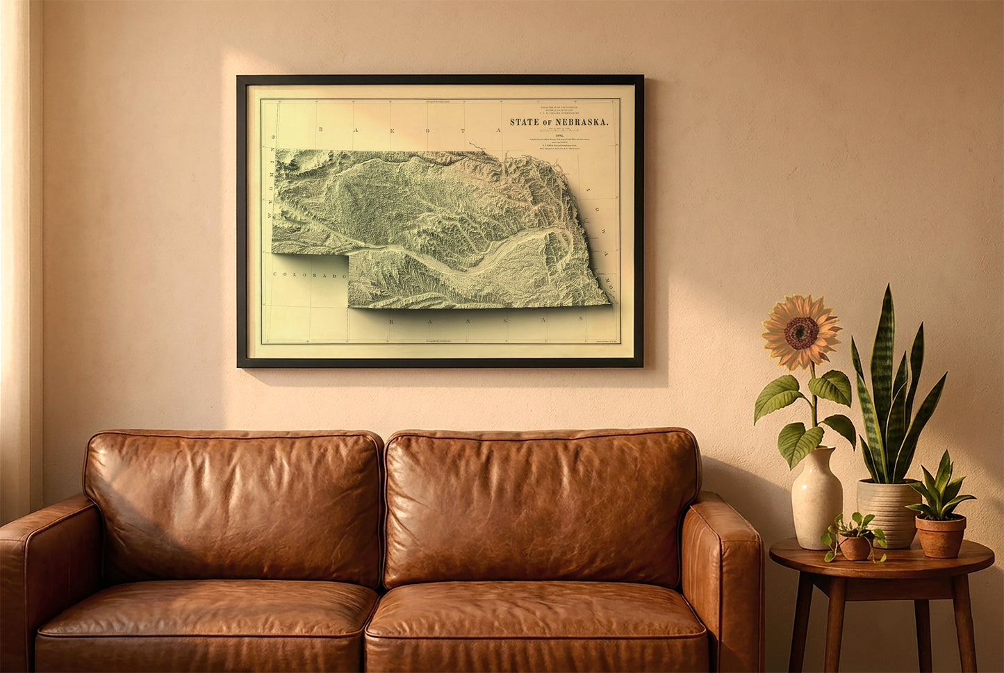 Nebraska vintage relief map in a black frame above a brown leather sofa. Boho living room with warm sunlight, sunflower, and indoor plants on a wooden side table