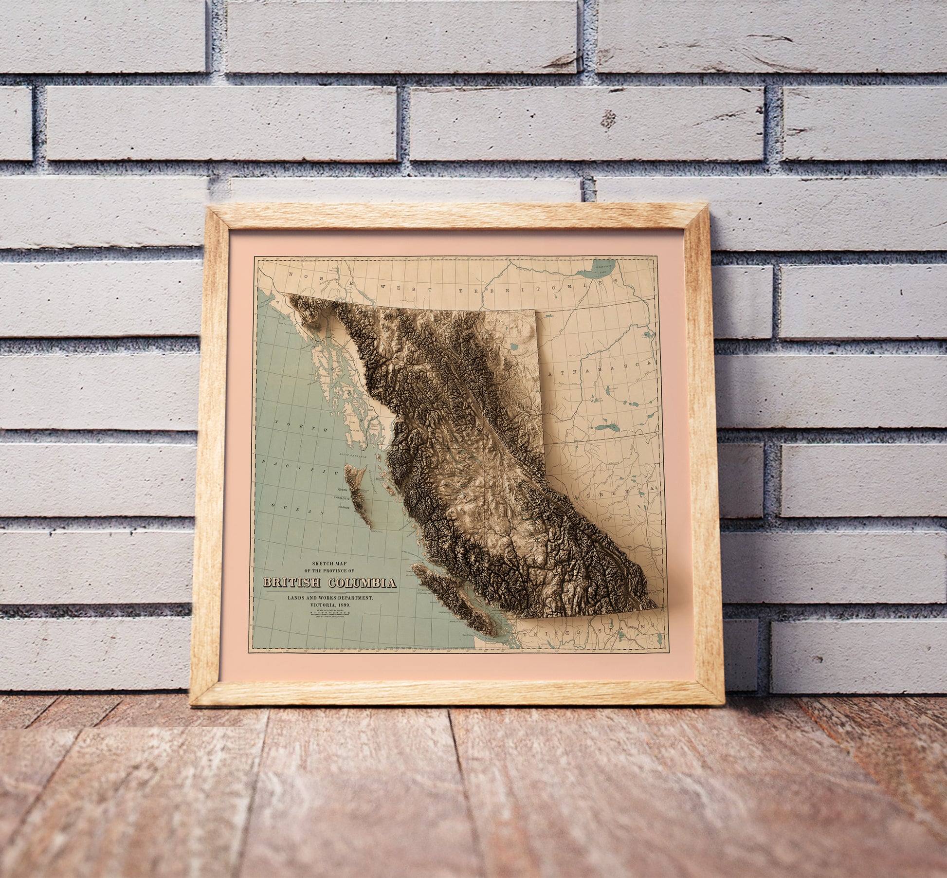 Vintage British Columbia, Canada, shaded relief map in a wooden frame. Realistic terrain art print for home decor, displayed against a brick wall