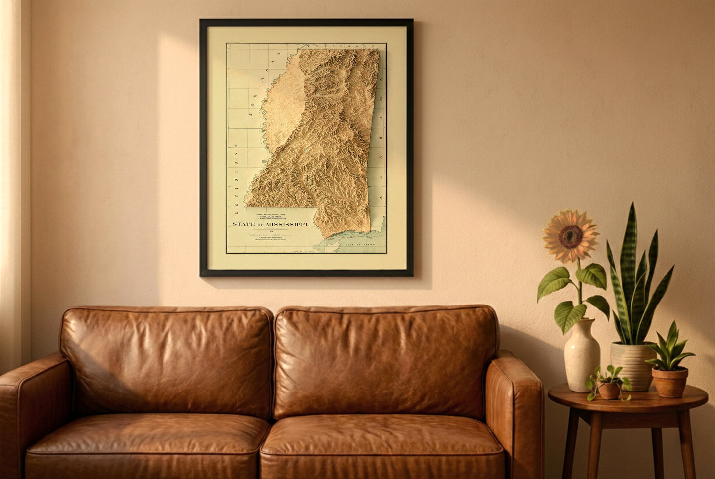 Mississippi vintage relief map in a black frame above a brown leather sofa. Boho living room with warm sunlight, sunflower, and indoor plants on a wooden side table