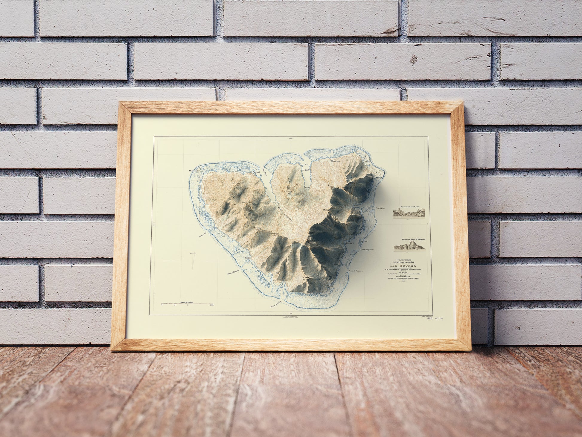 Vintage Moorea shaded relief map in a wooden frame. Realistic terrain art print for home decor, displayed against a brick wall