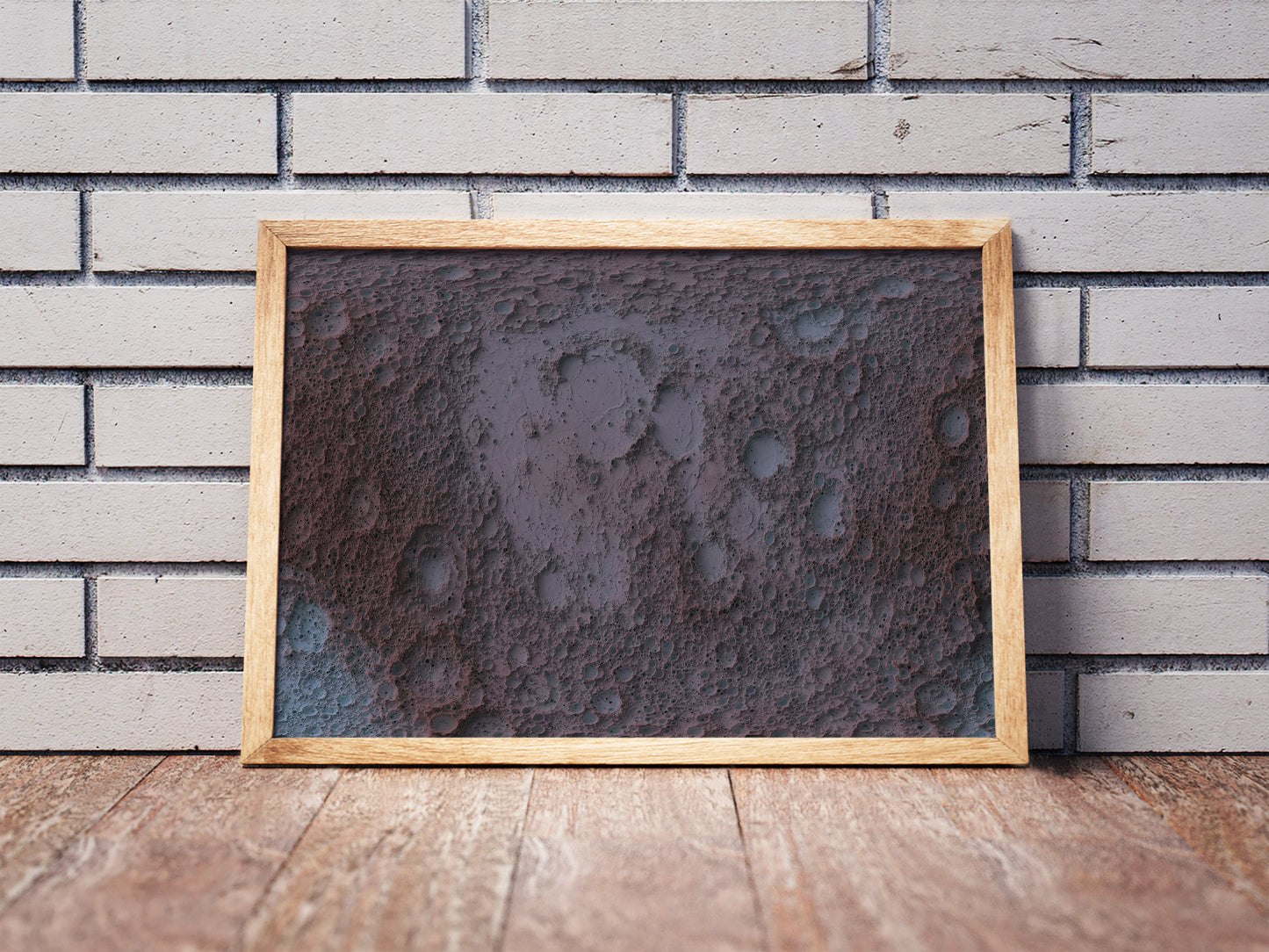 Moon shaded relief map in a wooden frame. Realistic terrain art print for home decor, displayed against a brick wall