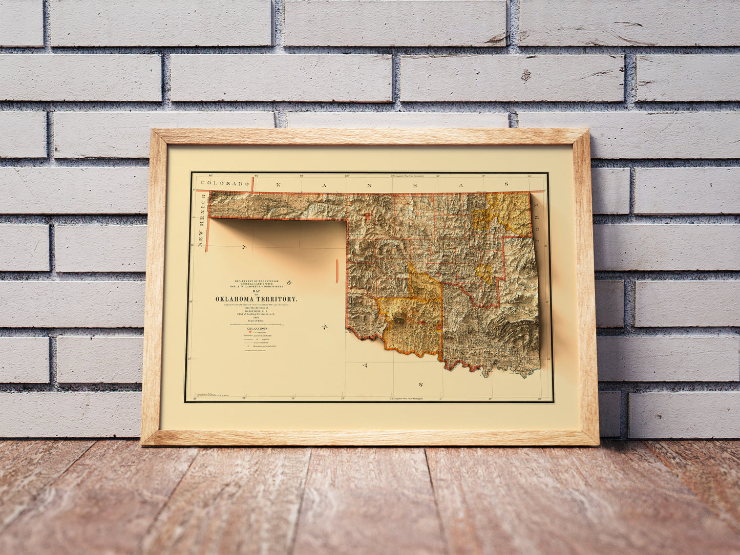 Vintage Oklahoma shaded relief map in a wooden frame. Realistic terrain art print for home decor, displayed against a brick wall