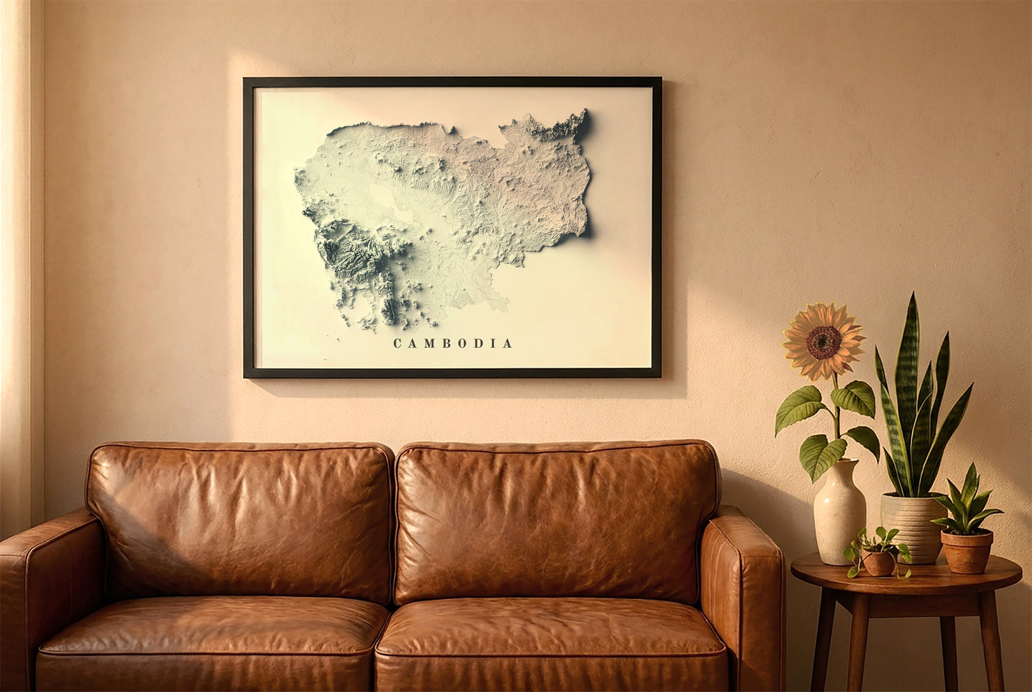 Cambodia relief map in a black frame above a brown leather sofa. Boho living room with warm sunlight, sunflower, and indoor plants on a wooden side table