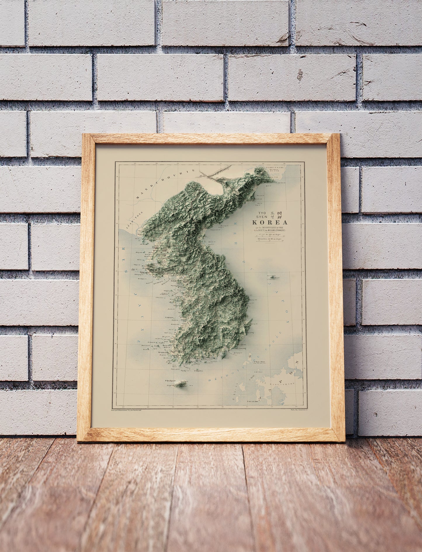 Vintage Koreas shaded relief map in a wooden frame. Realistic terrain art print for home decor, displayed against a brick wall