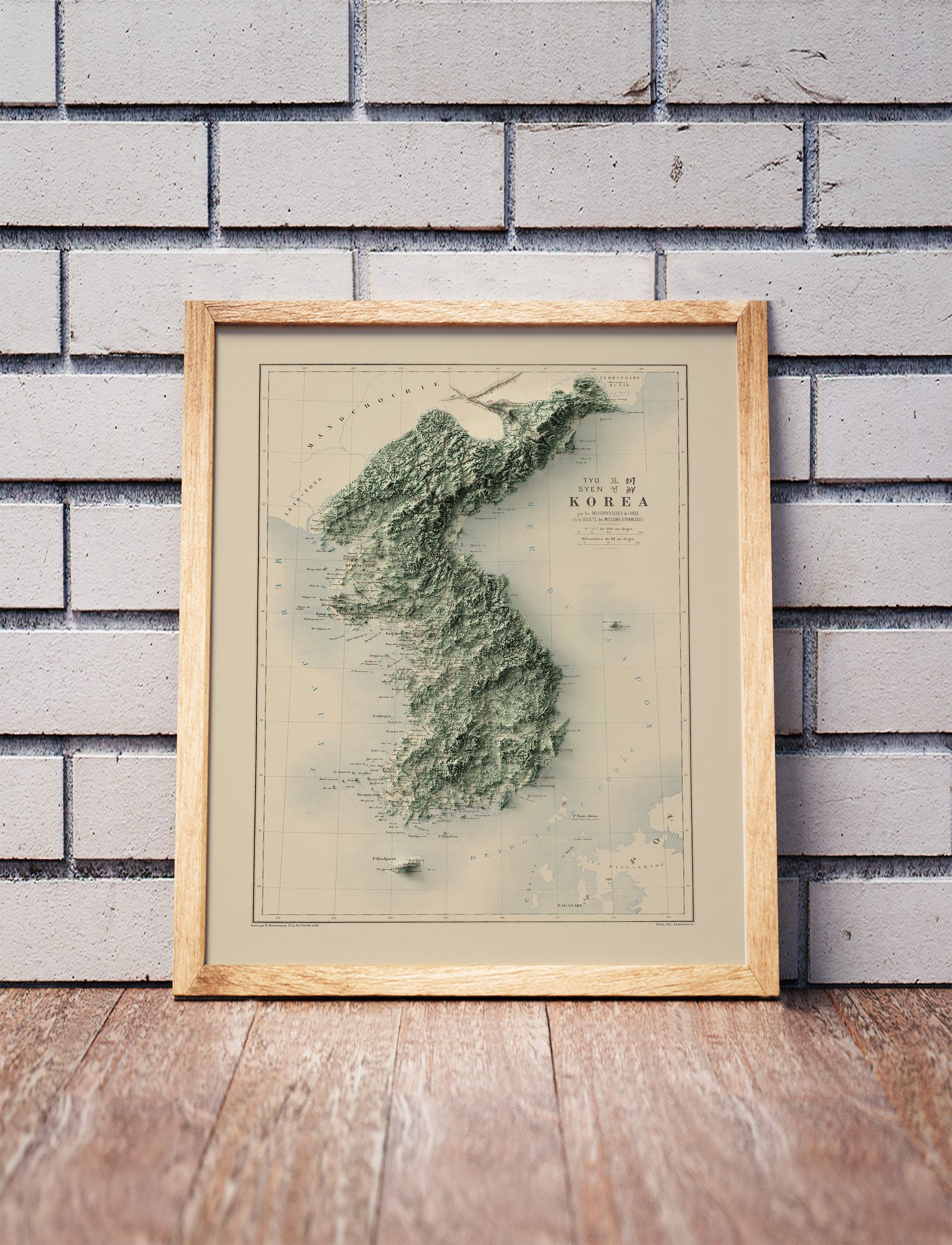 Vintage Koreas shaded relief map in a wooden frame. Realistic terrain art print for home decor, displayed against a brick wall