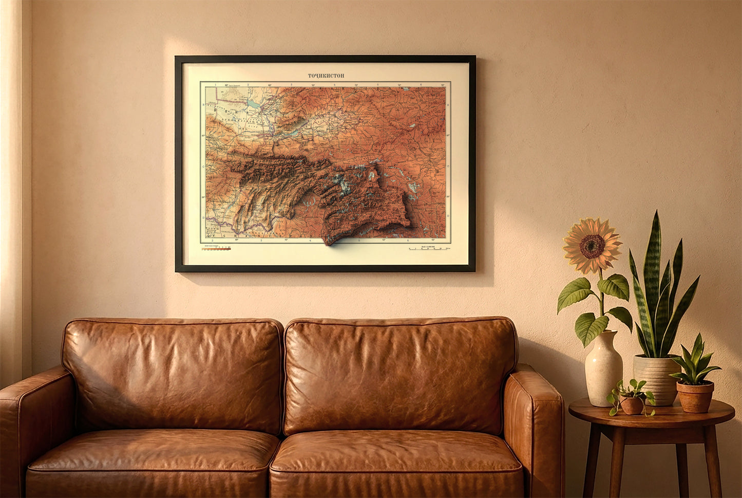 Tajikistan vintage relief map in a black frame above a brown leather sofa. Boho living room with warm sunlight, sunflower, and indoor plants on a wooden side table