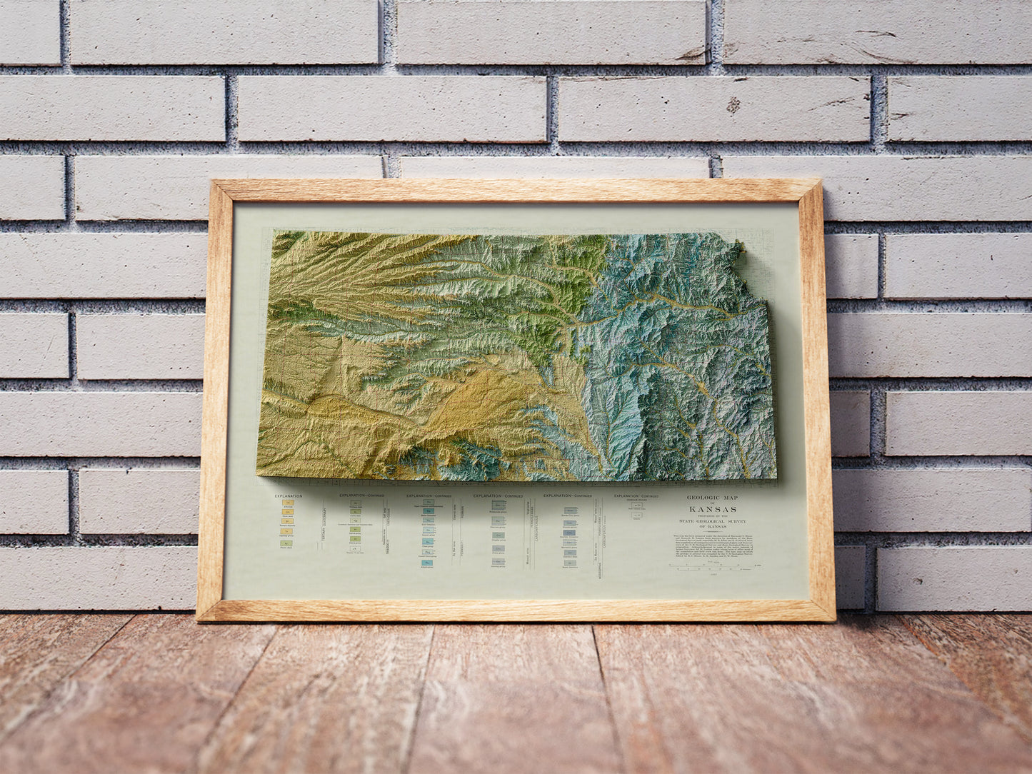 Vintage Kansas shaded relief map in a wooden frame. Realistic terrain art print for home decor, displayed against a brick wall